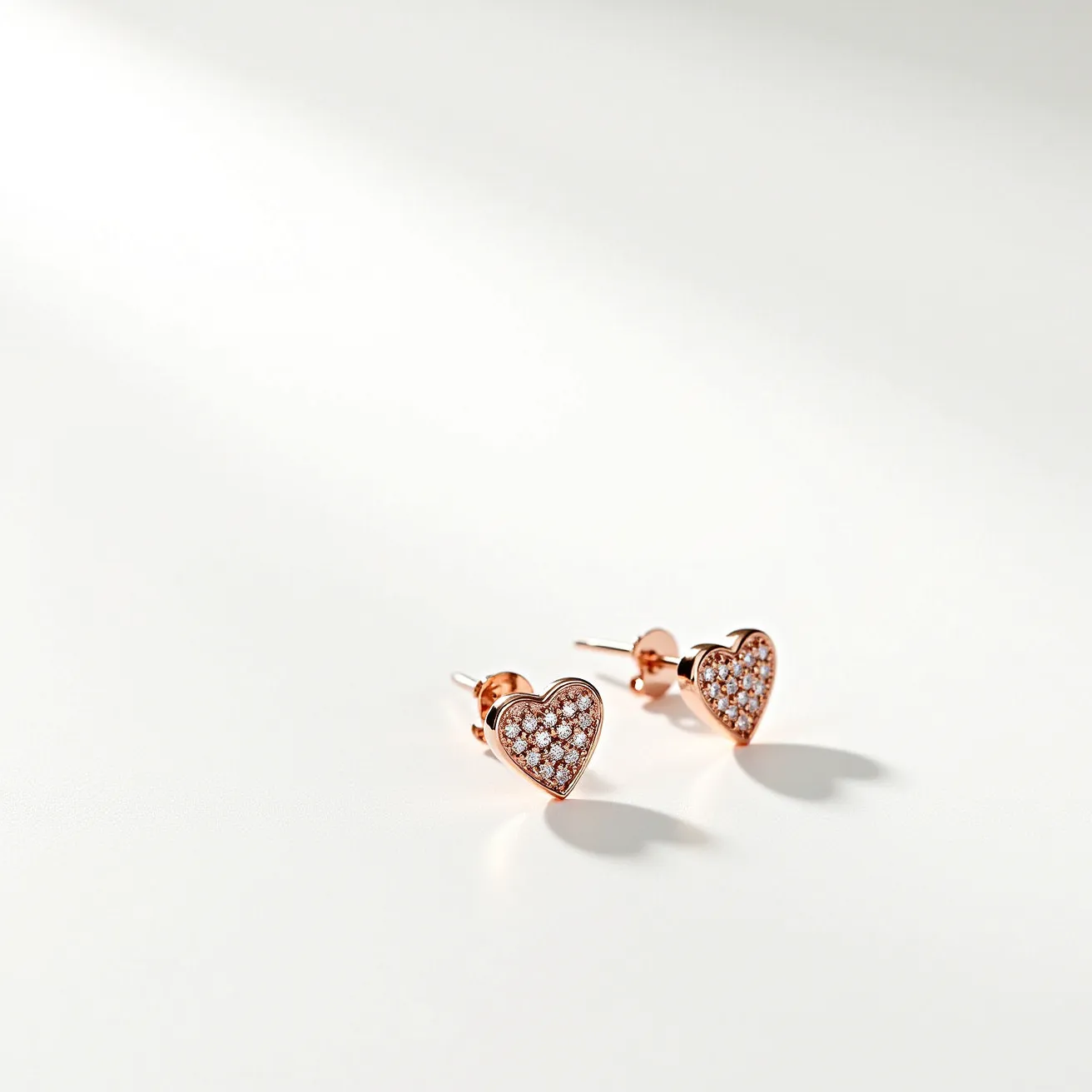 These heart earrings feature a charming design crafted from what appears to be a rose gold material, giving them a warm, elegant hue. The heart shapes are adorned with numerous small, round-cut gems, likely diamonds, which are pave-set across the entire surface, providing a shimmering effect. The earrings are held in place with a post and butterfly back, ensuring a secure fit when worn. The combination of the sparkling stones and the rose gold setting creates a sophisticated and timeless accessory.