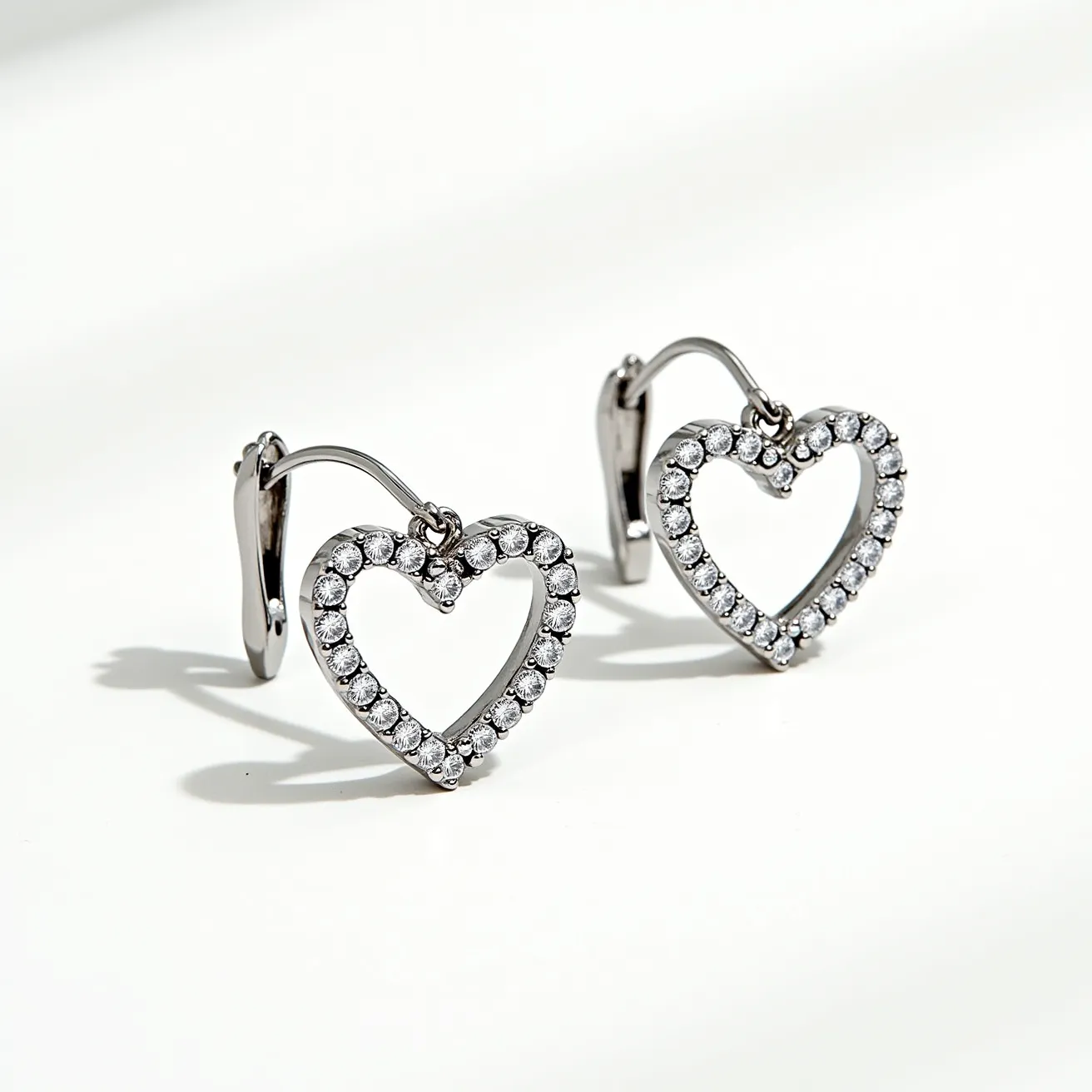 These heart earrings exhibit a delicate, open-heart design crafted from a shiny white metal, likely sterling silver or white gold, giving them a modern and elegant appearance. They are embellished with a series of small, round-cut clear gemstones, possibly diamonds or high-quality cubic zirconia, set in a pavé setting along the metal frame. These stones capture and reflect light effectively, enhancing the sparkle and allure of the earrings. The attachment features a lever-back clasp, ensuring secure and comfortable wear, while also adding a touch of sophistication to the design.