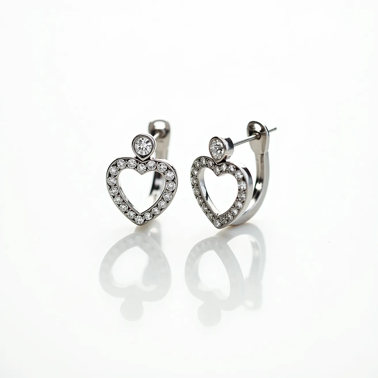 These heart hoop earrings feature a delicate design crafted from a lustrous metal, likely white gold or sterling silver, which forms the hoop and heart shapes. The hearts are embellished with small, round-cut clear stones, possibly diamonds or cubic zirconia, meticulously set in a pavé setting that enhances their sparkle. At the top of each heart, a larger, round brilliant-cut stone is prominently displayed, adding a focal point to the design. The earrings are equipped with a post and butterfly clasp attachment, ensuring secure wear and ease of use.