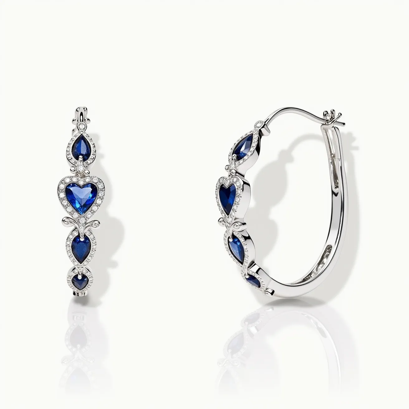 These heart hoop earrings are crafted from a polished metal, likely white gold or platinum, featuring a series of vibrant blue heart-shaped gemstones, presumably sapphires, which are prong-set along the hoop. Each heart-shaped sapphire is surrounded by smaller, round-cut clear stones, likely diamonds, in a pavé setting that adds a sparkling frame to the blue stones. The hoops utilize latch-back closures to ensure secure attachment, combining elegance with functionality. The alternating pattern and arrangement of gems create a visually striking effect, highlighting both the blue and clear stones prominently.