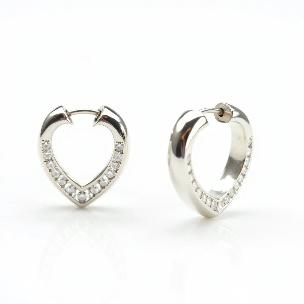 These heart hoop earrings are crafted in a sleek silver-tone metal, providing a lustrous and modern appearance. Embedded along the inner curve of the heart, a series of round-cut, clear stones are meticulously set, enhancing the earrings with a subtle sparkle. The stones are securely held in a pave setting, allowing each gem to catch and reflect light beautifully. The closure of the earrings is a hinged clasp, ensuring they are easy to wear and secure, making them both practical and stylish.