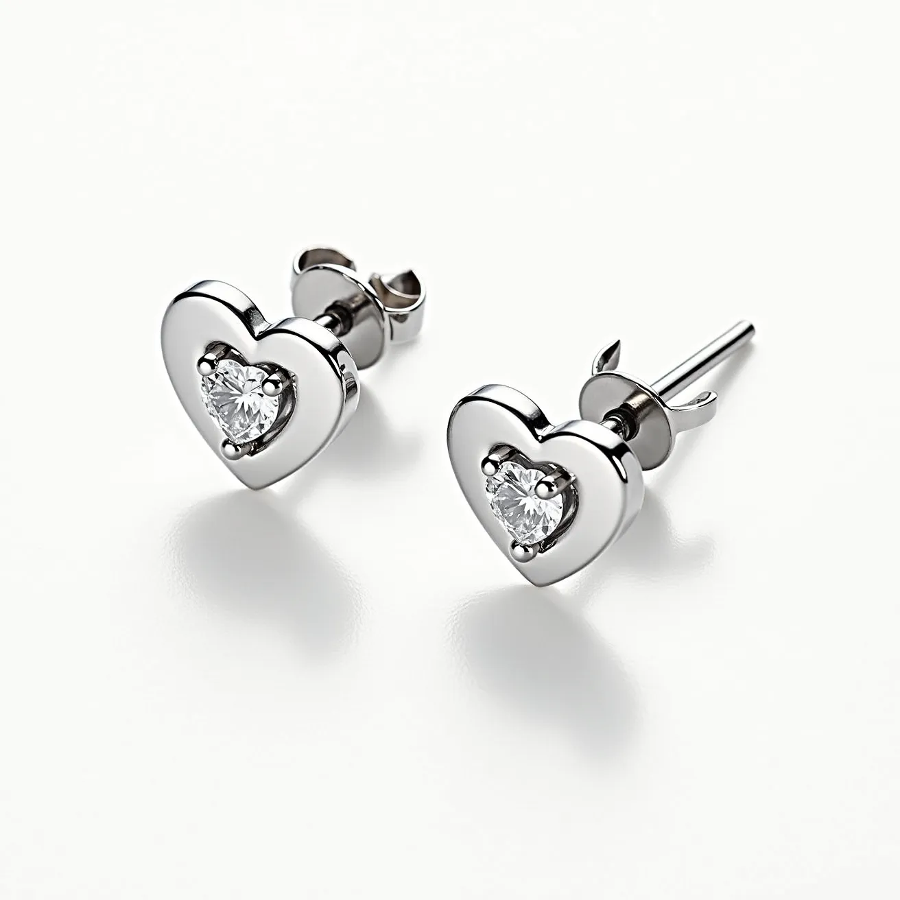 These heart stud earrings feature a sleek and polished metal setting, likely made of silver or white gold, that forms the shape of a heart. The center of each earring is set with a sparkling, heart-cut gemstone, which appears to be a diamond, securely held in place by a classic prong setting. This secure setting allows maximum light to pass through the stone, enhancing its brilliance and sparkle. The earrings are designed with a sturdy post and butterfly clutch back, ensuring they remain comfortably and securely fastened when worn.