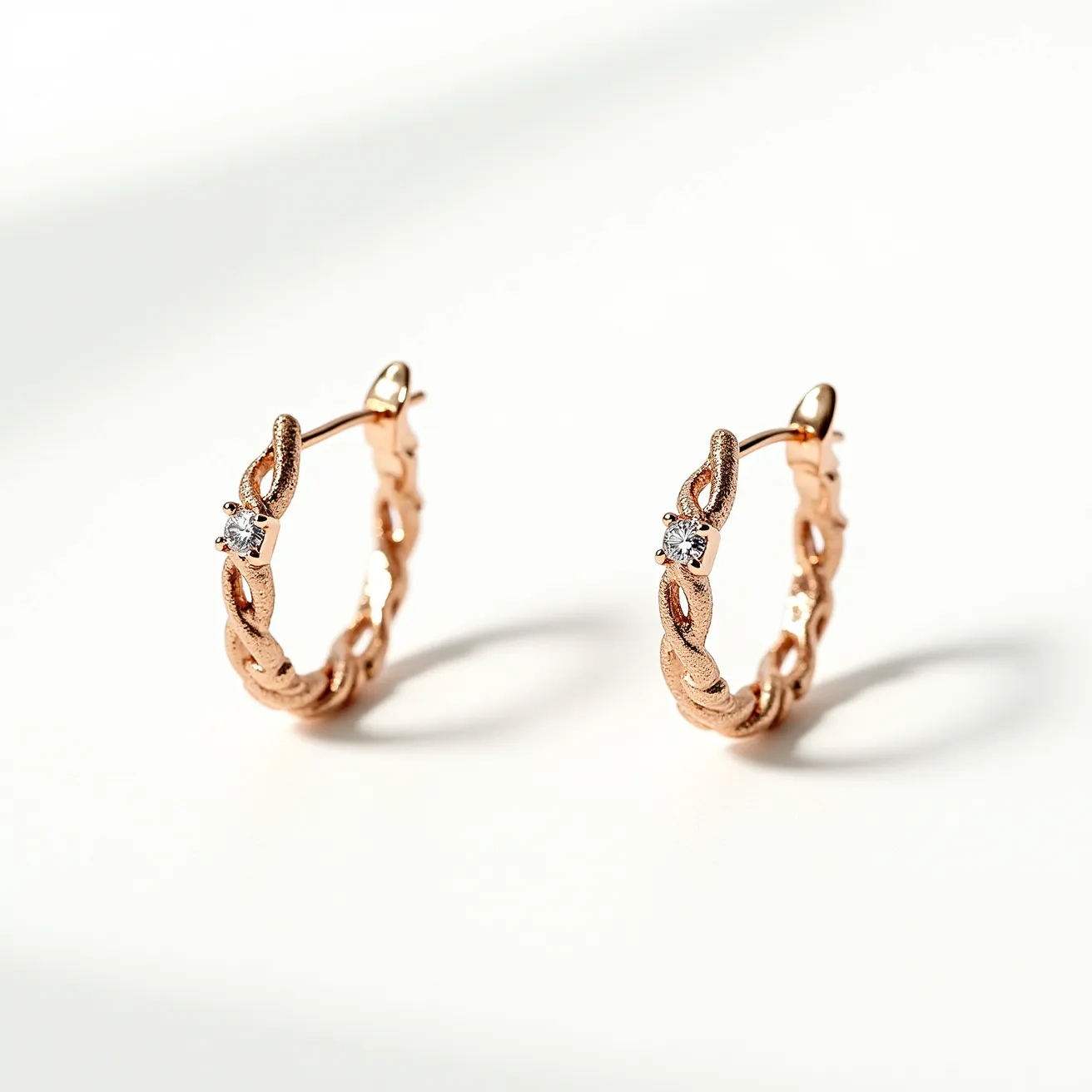 These helix hoop earrings feature a braided design made of a rose gold-toned metal, which adds an elegant texture and shine. Each earring is adorned with a single, clear gemstone, likely a round-cut diamond, secured in a prong setting. The earrings appear to fasten with a straightforward latch back closure, ensuring they remain securely in place when worn. The overall design is sophisticated and meticulously crafted, making it a stylish accessory for various occasions.