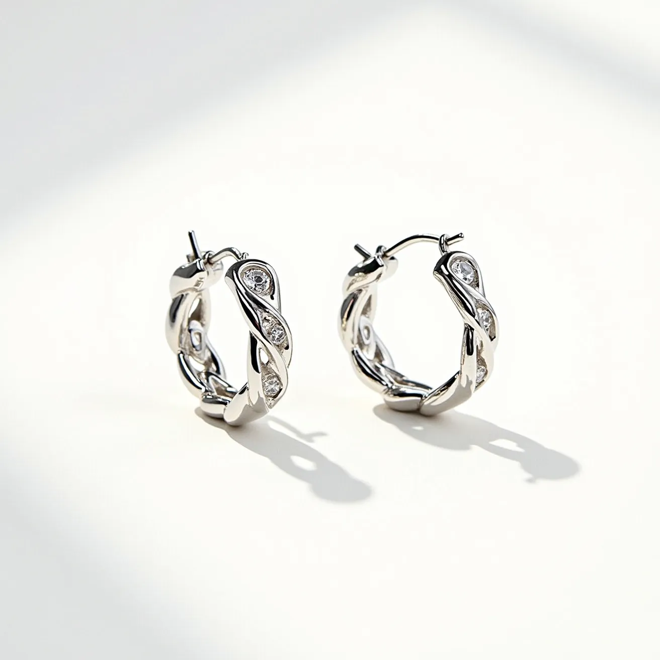 These helix hoop earrings exhibit a sophisticated intertwining design crafted from a shiny metal that appears to be silver or white gold. Embedded within the twisted structure are small, round-cut gemstones, likely diamonds, strategically set to enhance their brilliance and catch the light from various angles. The stones are held securely in place, possibly using a bezel or prong setting, which is subtly integrated into the design to maintain the elegant flow of the helix pattern. The earrings feature a hinge and latch backing mechanism, ensuring a secure and comfortable fit when worn.