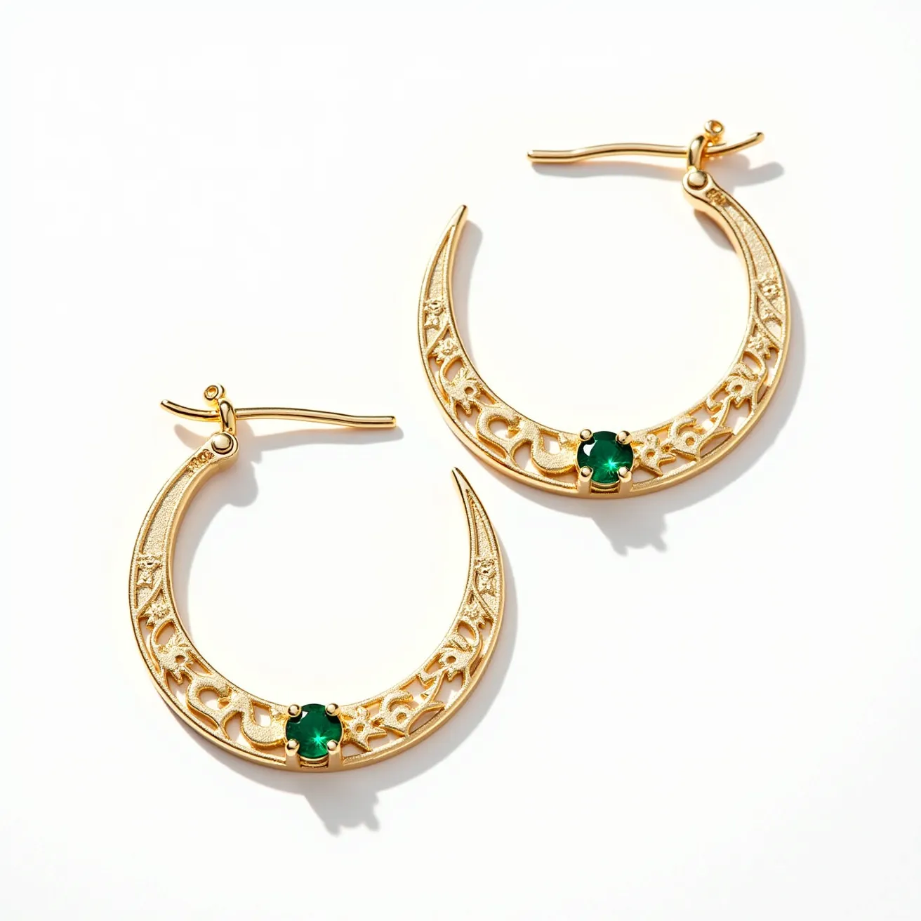 These hoop earrings feature a crescent shape crafted from gold, showcasing intricate filigree detailing along the curved body. Each earring is adorned with a round green gemstone set in a prong setting at the base of the crescent, adding a touch of elegance and color contrast. The earrings are equipped with a secure latch back clasp for easy and secure fastening. These elements together create a striking balance of traditional design and modern aesthetic.