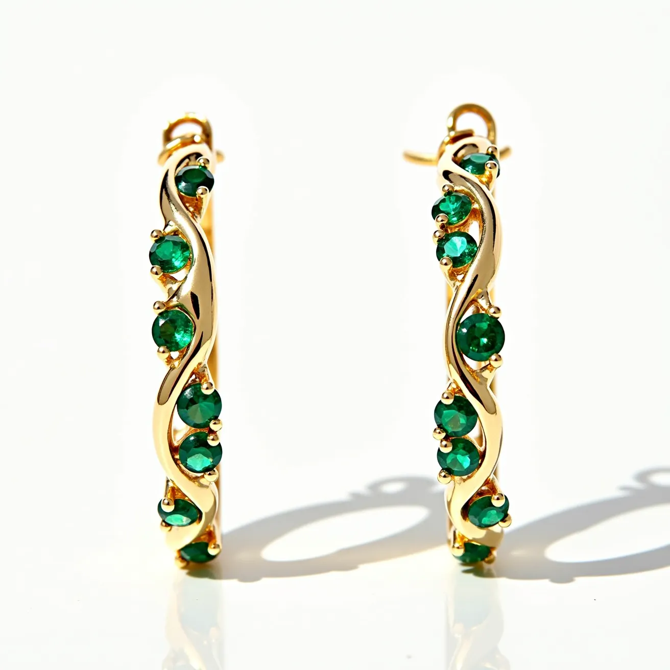 These hoop earrings feature a luxurious gold metal structure with an intricate twisted design. Adorned with round-cut green gemstones, likely emeralds, each stone is securely nestled in a prong setting that complements the elegant curves of the metal. The design exudes a sense of sophistication, with the vibrant green stones adding a striking contrast to the warm gold. The earrings are equipped with a classic hinged clasp, ensuring they are both secure and easy to wear.