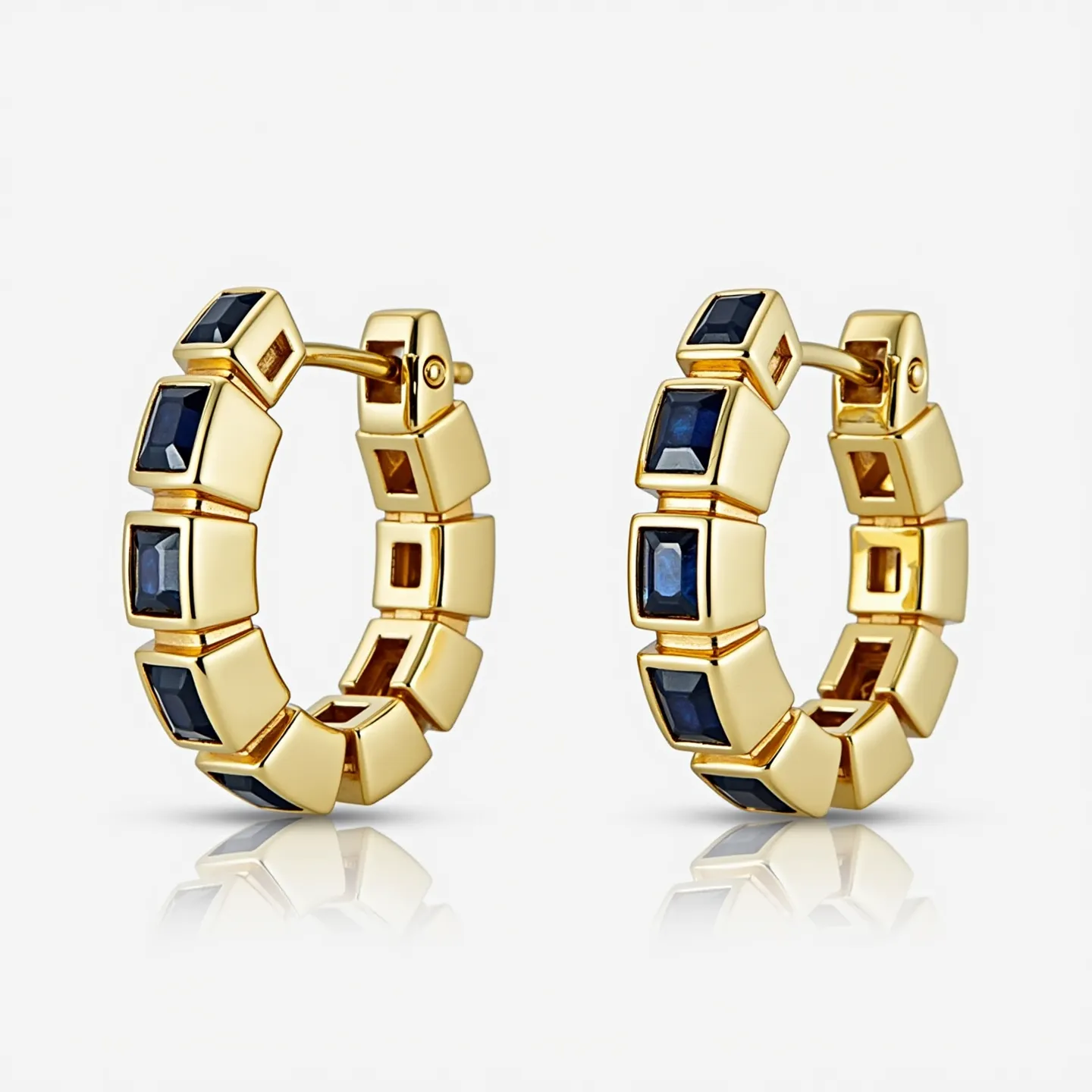 These huggie earrings feature a polished gold setting that showcases a series of square-cut blue stones, likely sapphires, which are elegantly embedded along the circumference. The stones are set in a bezel-style that accentuates their color and clarity, providing a sophisticated contrast against the warm gold. The earrings utilize a hinged clasp mechanism, ensuring a secure and convenient attachment. The geometric design and luxurious materials highlight a modern yet timeless aesthetic, suitable for both formal and casual occasions.