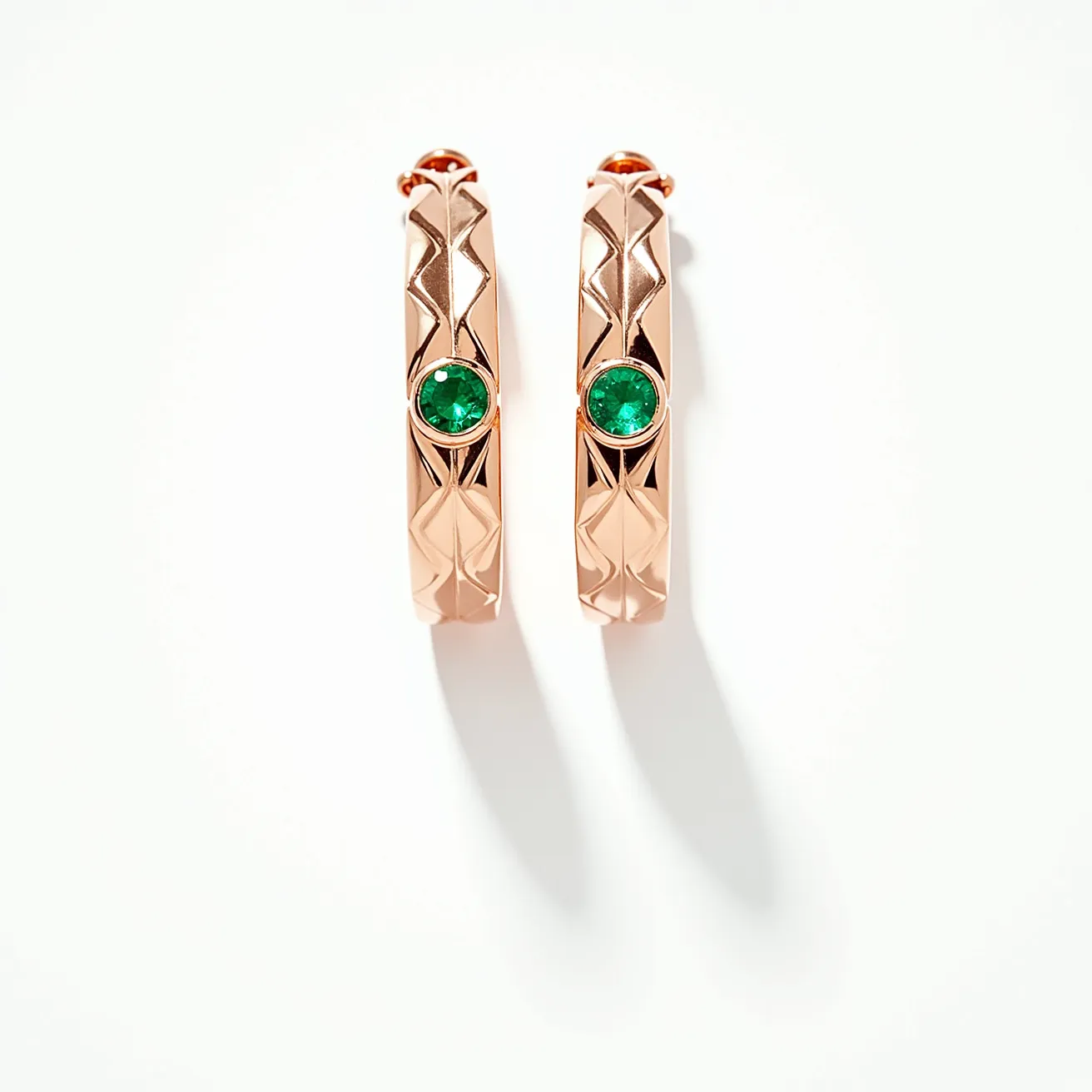 These huggie earrings are crafted from a polished gold material, featuring a geometric design that adds a modern touch. Each earring showcases a single round-cut green gemstone, likely an emerald, set in a bezel setting that secures the stone while highlighting its vibrant color. The earrings have a hinged closure that ensures they fasten securely and comfortably around the earlobe, making them both elegant and practical for everyday wear.