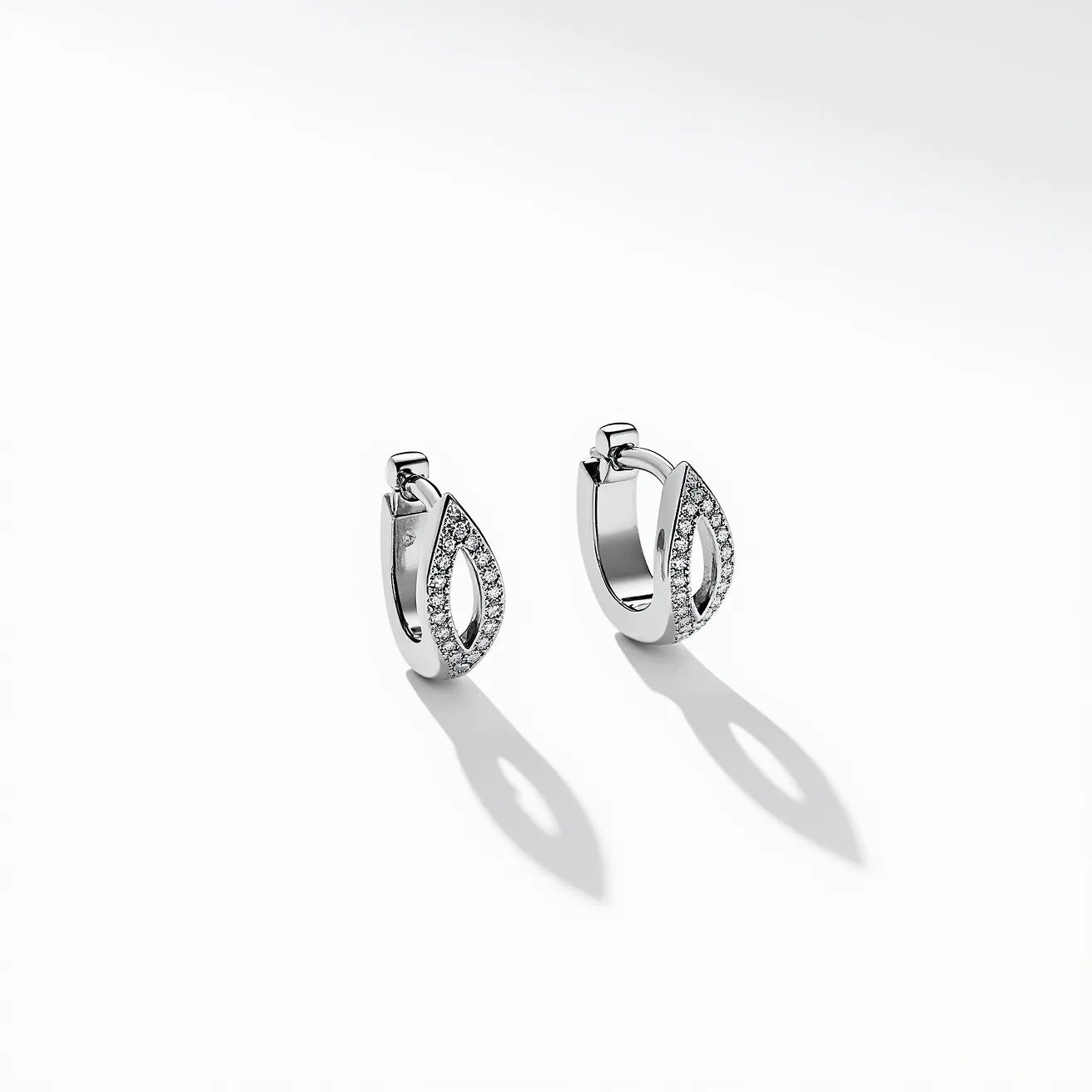 These huggie earrings are crafted from a polished silver-toned metal, featuring an elegant open teardrop design. Each earring is adorned with a series of small, round, clear gemstones, likely diamonds or cubic zirconia, which are pavé set along the front side of the hoop and the teardrop. The earrings are designed to fasten securely with a hinged clasp, a common feature in huggie styles, allowing them to hug the earlobe closely for a sleek and sophisticated look. The combination of the metallic sheen and sparkling stones gives these earrings a refined, luxurious appearance.