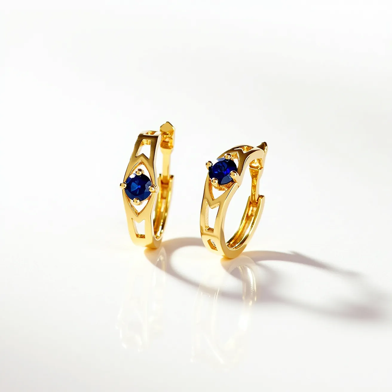 These huggie earrings pair is crafted from gold, featuring a sleek, polished finish. Each earring is adorned with a single round-cut blue gemstone, likely sapphire, securely set in a prong setting that allows the gem to catch light effectively. The earrings have a small hinged clasp that facilitates easy attachment to the ear, ensuring a snug fit. The open design on the band adds a modern aesthetic to this classic hoop style.