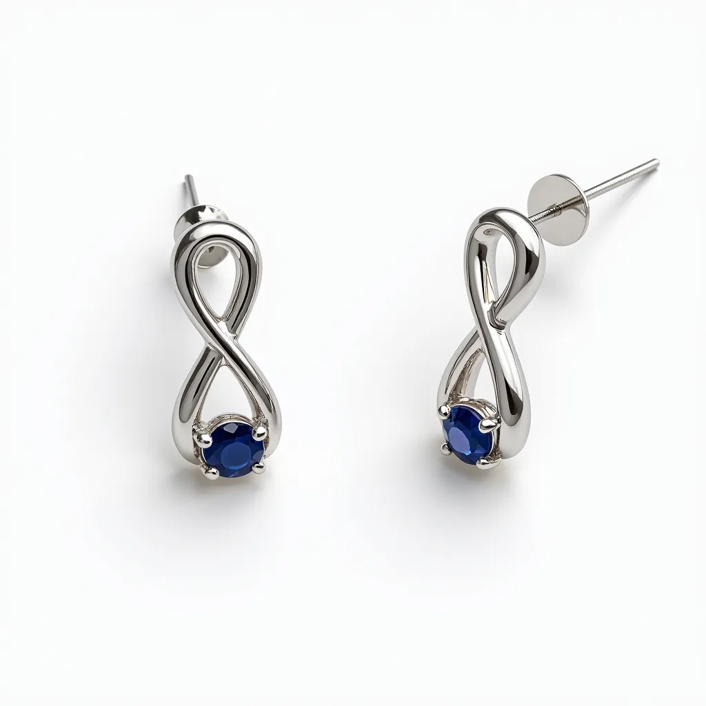 These infinity earrings feature a sleek design crafted from a polished silver-tone metal, forming a classic infinity loop. At the base of each piece lies a brilliant blue gemstone, likely a sapphire, in a round cut, adding a striking pop of color. The gems are secured in a prong setting, enhancing their visibility and sparkle. These stud earrings are equipped with post back attachments, ensuring a secure fit when worn. Combining elegance and simplicity, they make a timeless addition to any jewelry collection.