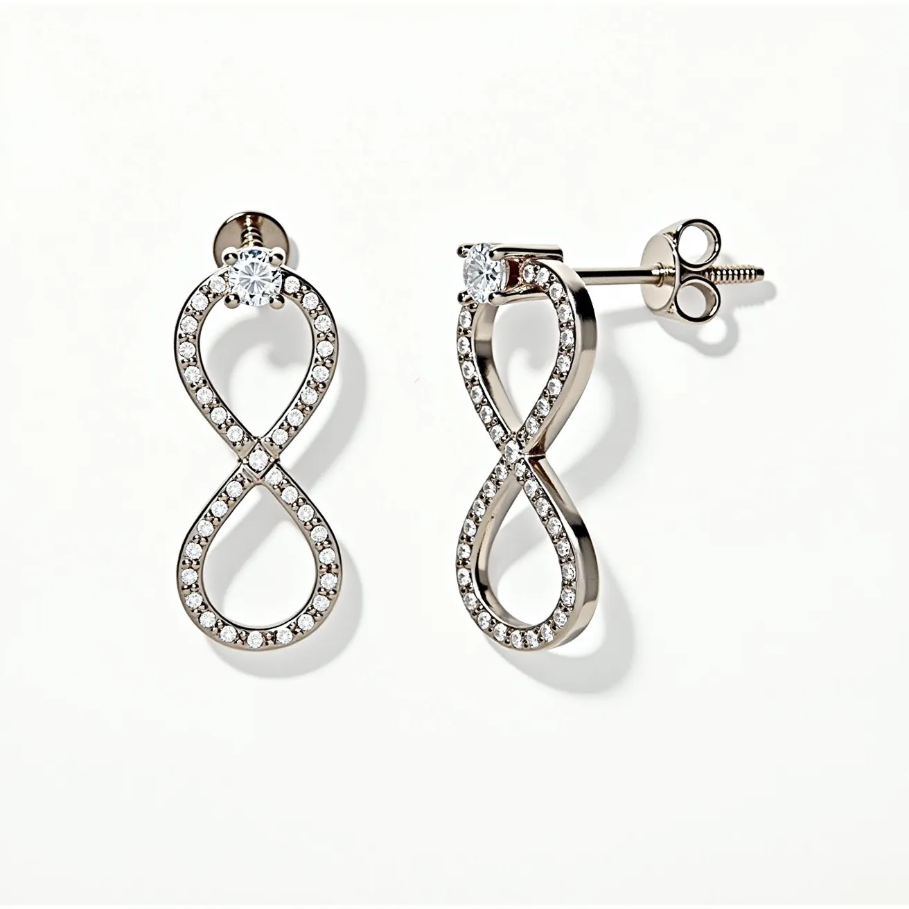 These infinity earrings design features a sleek and polished metal structure forming the iconic infinity symbol. The earrings are adorned with small, round, brilliant-cut clear gemstones, likely set in a pavé style along the entire loop, adding a sparkling accent to the piece. At the top of each earring, a larger round gemstone is set in a prong setting, enhancing its brilliance. The attachment consists of a post and butterfly clasp, ensuring they are secure and easy to wear.