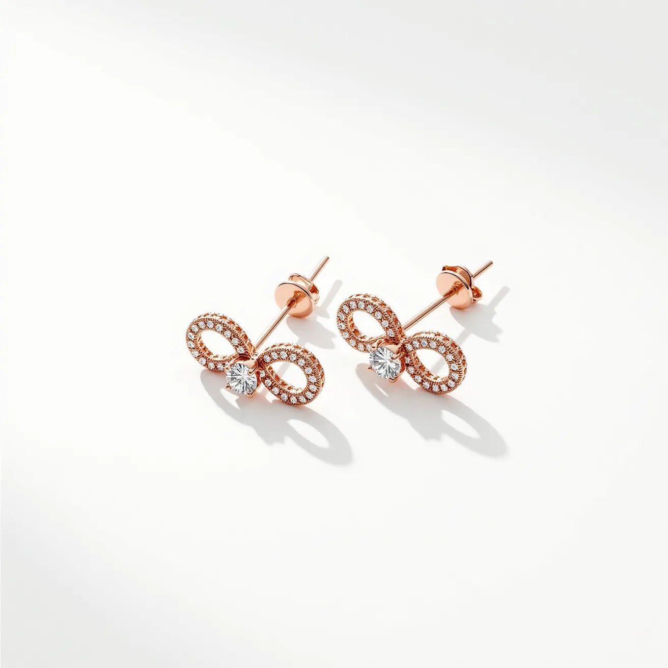 These infinity earrings feature a striking design crafted from a warm rose gold material, which forms the iconic infinity symbol. Each earring is embellished with small, sparkling diamonds that are pavé set, enhancing the elegance of the motif. At the center of the infinity loop, there is a larger round brilliant-cut diamond set in a secure prong setting, adding a focal point of brilliance. The earrings use a simple post and butterfly back attachment, ensuring ease of wear and a secure fit. The overall design exudes sophistication and timeless appeal.