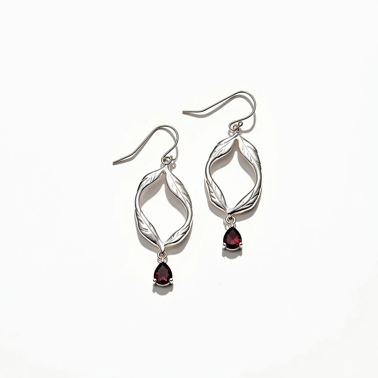 These leaf earrings feature a delicate leaf motif crafted from a silver-toned metal, giving an elegant and naturalistic appeal. The design is further enhanced by a single teardrop-shaped red gemstone, likely a garnet, which is securely prong-set at the bottom of each earring. The earrings are equipped with hook clasps, providing a simple yet effective means of attachment. The overall design harmonizes organic forms with a touch of sophisticated sparkle, making them versatile for various occasions.