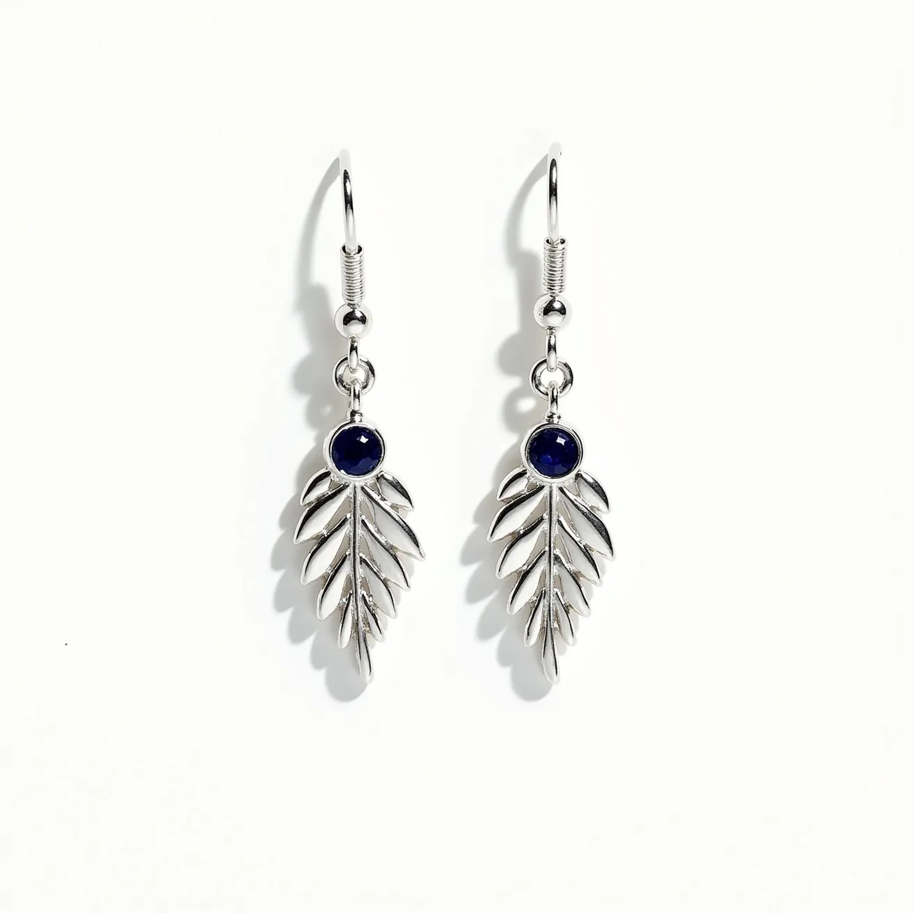 These leaf earrings feature a sleek metal design, likely crafted from silver or a similarly polished material, shaped into intricate leaf patterns. At the top of each leaf is a deep blue gemstone, set in a bezel setting that securely holds the round-cut stones, adding a touch of elegance and contrast to the metallic sheen. The earrings are attached to smooth, curved hooks, commonly known as French hooks, which provide a classic and easy-to-use mechanism for wearing. The overall aesthetic blends natural inspiration with refined craftsmanship, making these earrings a striking accessory.