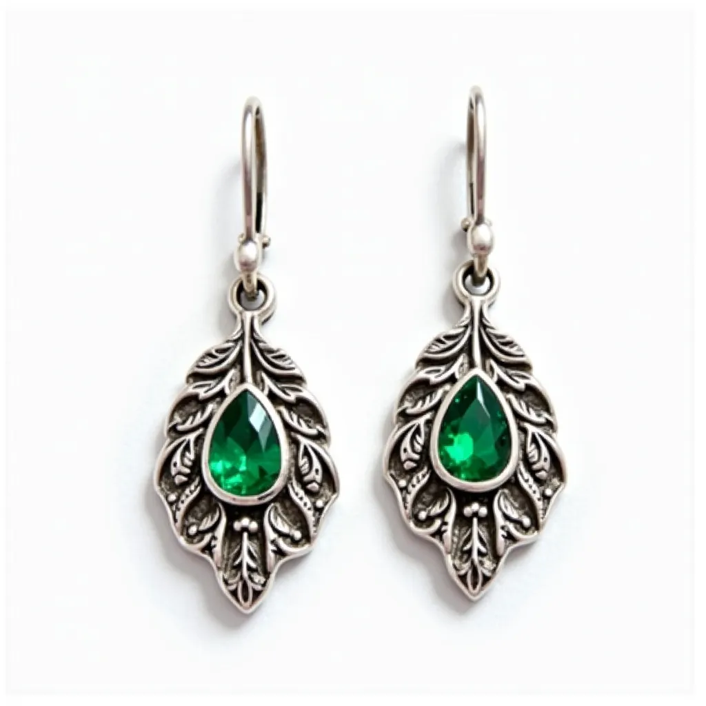 These leaf earrings feature an intricate leaf design crafted from a metallic material with an antique finish. Each earring is embellished with a pear-cut green gemstone, set in a bezel setting, which adds a vibrant contrast to the metallic backdrop. The detailing on the leaves includes delicate etchings that enhance the organic look of the piece. The earrings are designed with a French hook clasp, providing a secure and elegant attachment. This combination of materials and craftsmanship results in a striking, nature-inspired accessory.