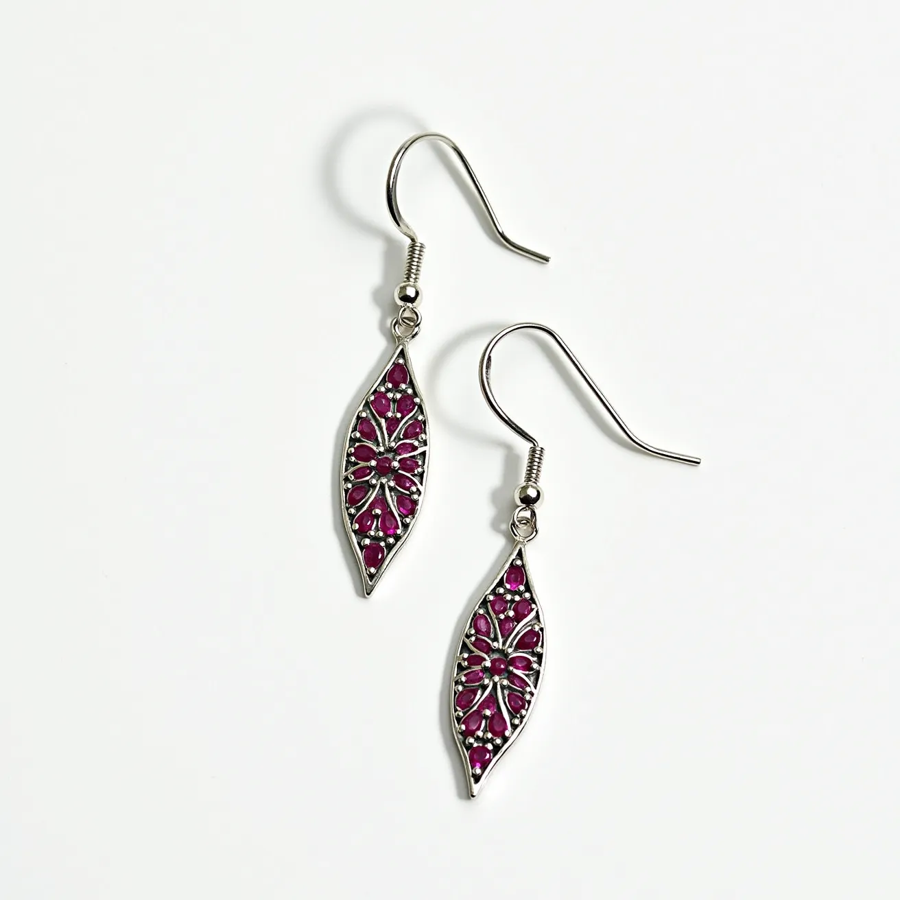 These leaf earrings feature a slender, elongated design resembling the shape of a leaf, delicately crafted from a silver-toned metal. Embedded within the metal framework are numerous small, round red gemstones that fill the interior with a vibrant and lively color, arranged in a symmetrical pattern that adds a floral-like texture to the design. The stones are securely set in place, though the specific setting style is not precisely defined. The earrings are designed with a fish hook clasp, allowing for easy and comfortable wear, complementing the elegant and sophisticated appearance of the leaf motif.