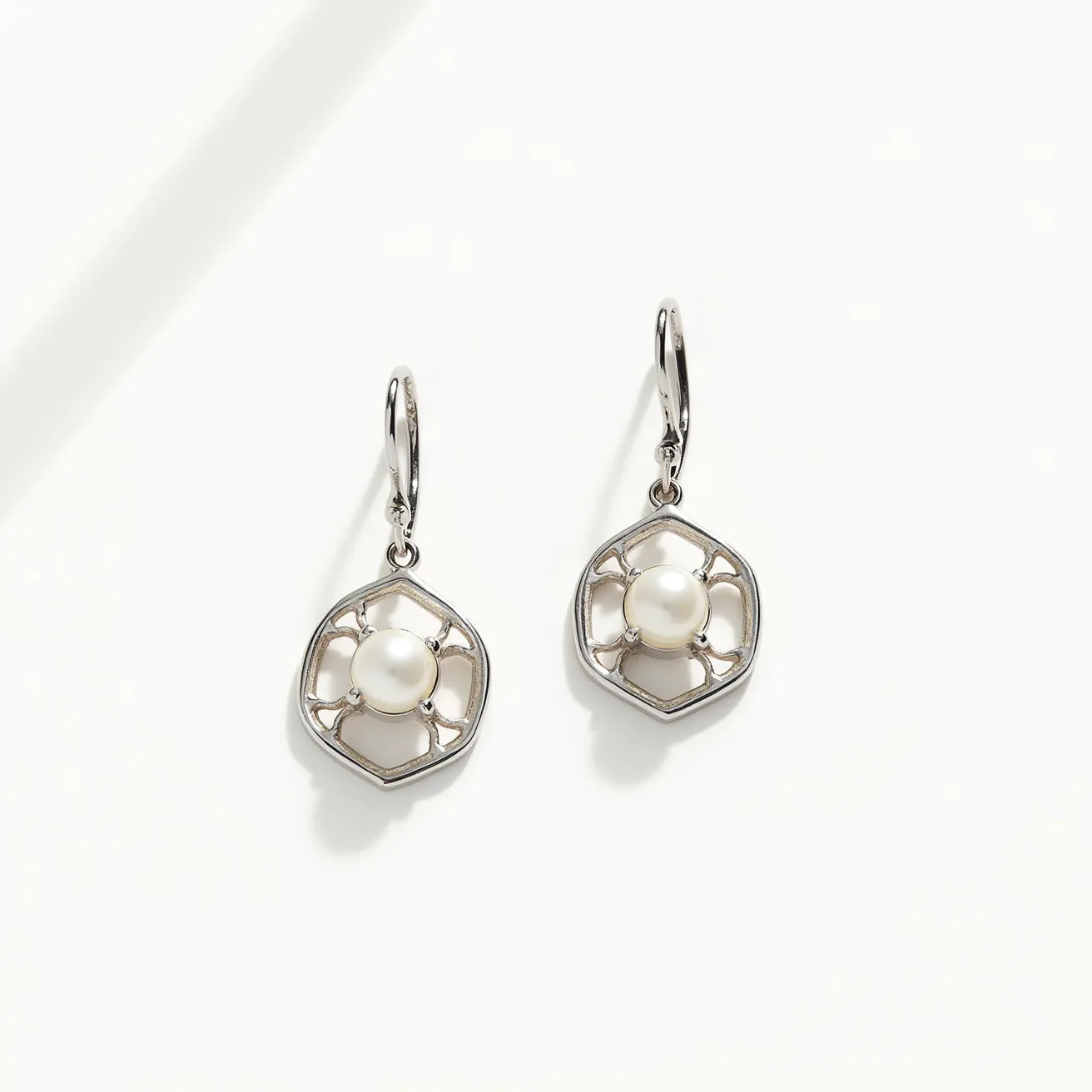 These leverback earrings showcase a sophisticated design featuring a round, lustrous pearl at the center of each earring, likely set in a prong setting to accentuate its elegant appearance. The pearl is encircled by a delicate and intricately designed metal framework, possibly made of silver or white gold, adding a modern touch to the vintage-inspired structure. The metal framework is shaped in a hexagonal pattern, contributing to a geometric aesthetic that complements the smooth, organic texture of the pearl. The earrings are equipped with a secure leverback clasp, enhancing comfort and ease of wear while ensuring they stay securely fastened.