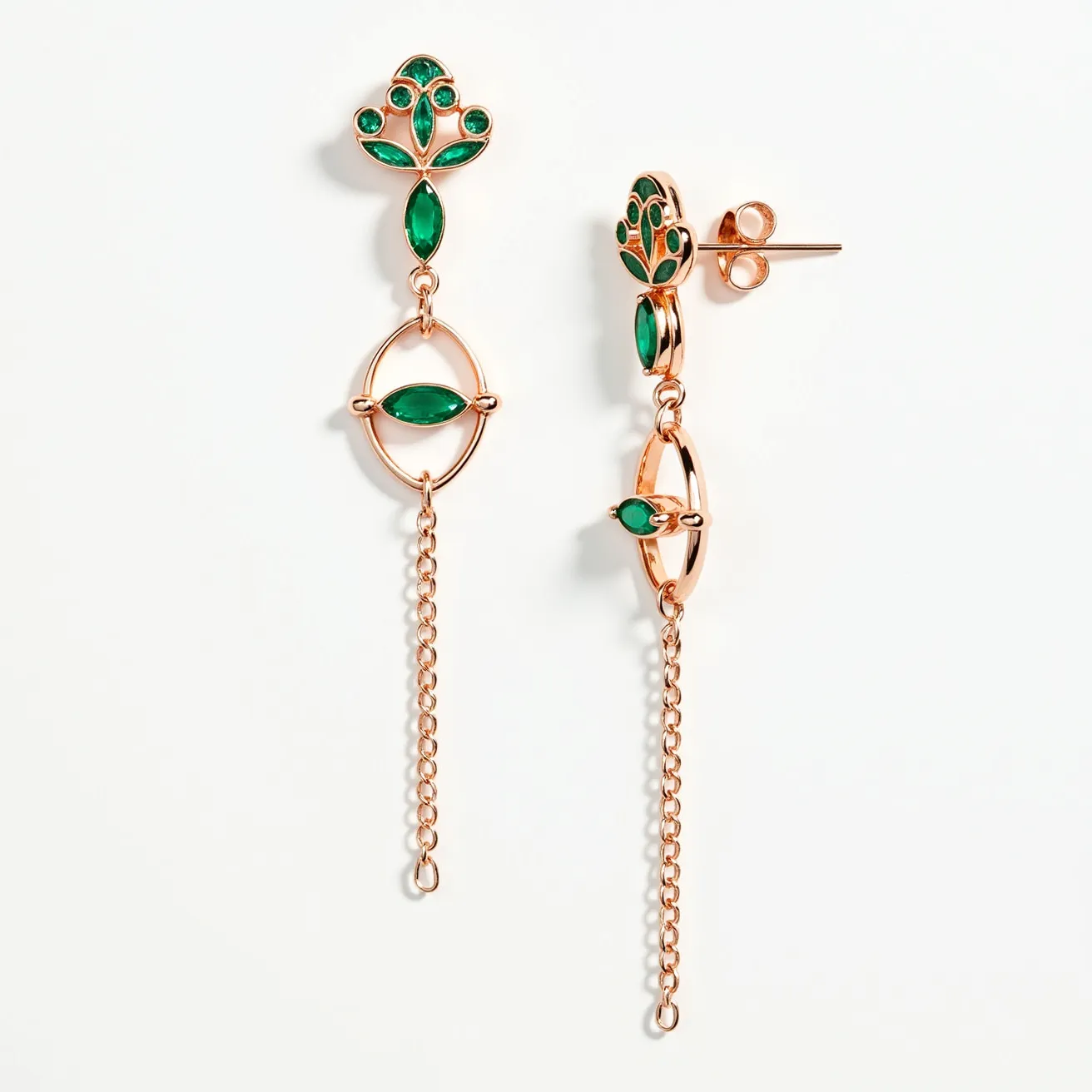 These long earrings feature a combination of gold-toned metal and vivid green stones. The upper part displays a tree-like design embellished with round and marquise-cut gems, presumed to be emeralds, set in a simple prong setting. The centerpiece is an elegant oval frame that houses a singular marquise-cut stone, mirroring the stones above. From the oval frame hangs a delicate chain, adding an elongated and graceful element to the design. The earrings are secured with a post and butterfly backing, ensuring a snug fit and ease of wear.