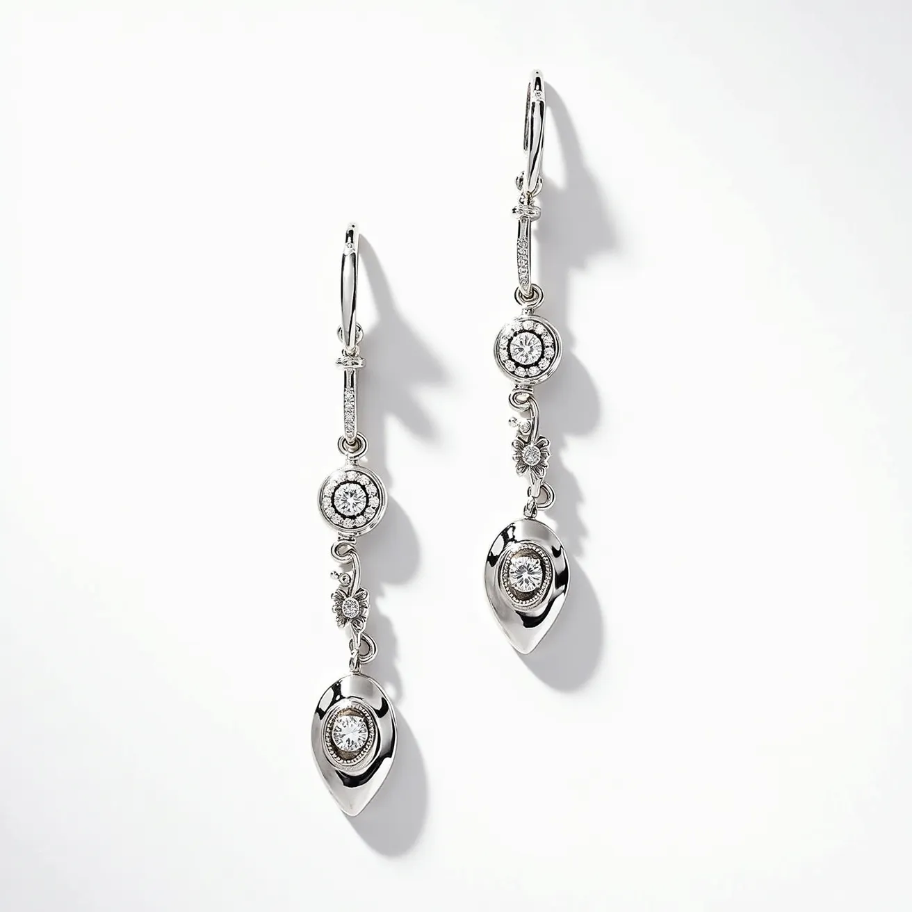 These long earrings are crafted from a shiny metallic material, likely silver or white gold, featuring an elegant design with multiple components. The earrings include multiple gemstones, with round, brilliant-cut stones centrally set in a bezel setting, adding both sparkle and elegance. Small floral or abstract motifs adorn the space between the stones, contributing to the elaborate design. The earrings conclude with a teardrop-shaped component, also featuring a centrally set stone, enhancing the overall sophistication. They are equipped with lever-back clasps, providing secure attachment while maintaining comfort.