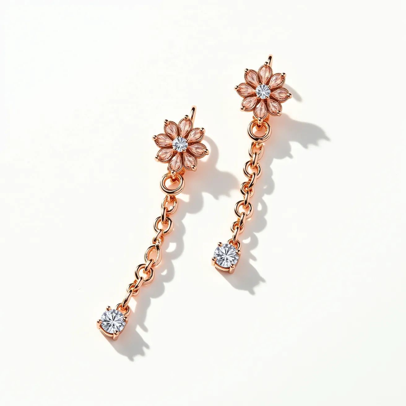 These long earrings display a delicate design crafted from a rose gold-toned metal, featuring a floral motif with a central round-cut clear gemstone, likely a cubic zirconia, set in a prong setting. Each earring extends into a dangling chain link that culminates in another round-cut clear gemstone, similarly set in a prong setting. The earrings attach via a simplistic hook clasp that ensures a secure fit while accentuating the overall elegant design.