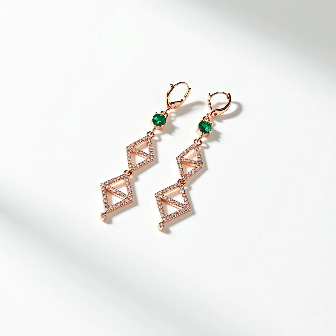 These long earrings feature a striking design crafted in a rose gold-toned metal, creating an elegant and modern look. Each earring showcases a vibrant, round-cut green gemstone, likely emerald, set in a prong setting that enhances its captivating color. The earrings are adorned with geometric, rhombus-shaped links embellished with small, clear, round-cut stones, possibly diamonds or cubic zirconia, set in a pave style that adds a subtle sparkle. The earrings are equipped with lever-back clasps, ensuring a secure and comfortable fit when worn.