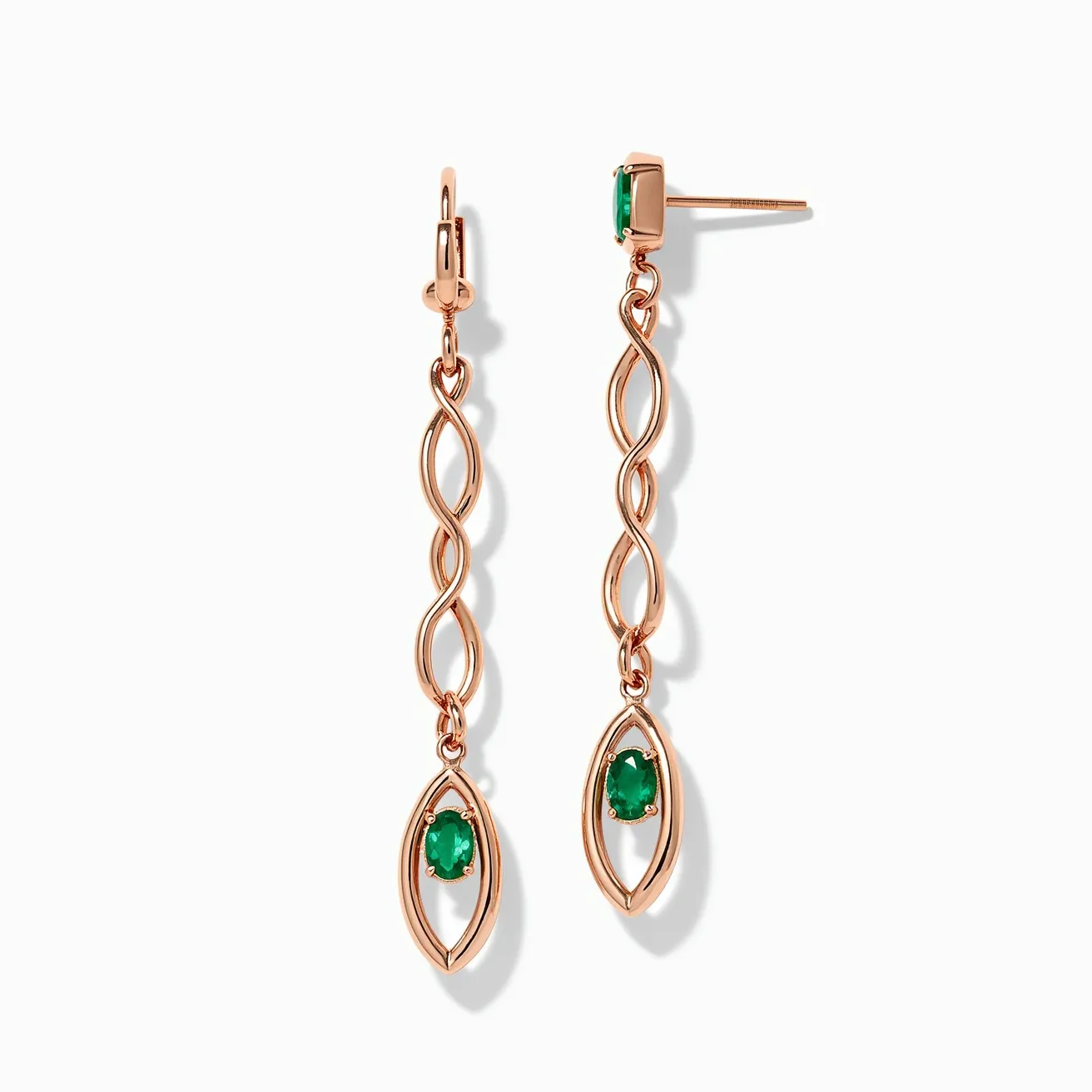 These long earrings feature an elegant design crafted from a rose gold-toned metal that forms flowing, open loops down the length of the piece. At the end of the earring, there is an eye-shaped frame holding an oval-cut green gem, possibly an emerald, set in a prong setting. The gem's vivid hue contrasts beautifully with the warm metallic tones. The earring utilizes a hook-style clasp on one piece and a standard post with a friction back on the other, providing secure attachment options. The combination of the intricate metalwork and vibrant gemstone creates a sophisticated and timeless aesthetic.