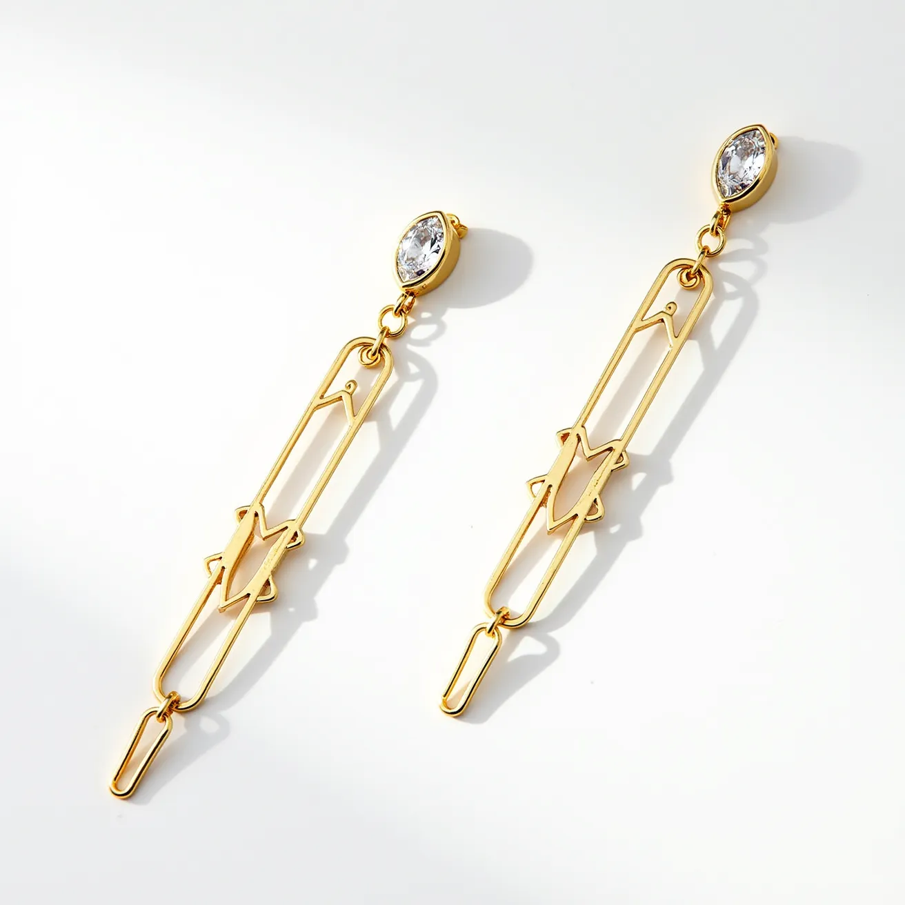 These long earrings feature an elegant design crafted from a gold-toned metal, giving them a sleek and modern appearance. At the top, a marquise-cut clear gem is set in a simple bezel setting, adding a touch of sparkle and elegance to the overall look. The elongated structure is characterized by a geometric pattern with open spaces, creating an intricate visual interest. The earrings are connected with small links, allowing for gentle movement. An easy-to-use hook or post-back fixture ensures secure attachment to the ear.