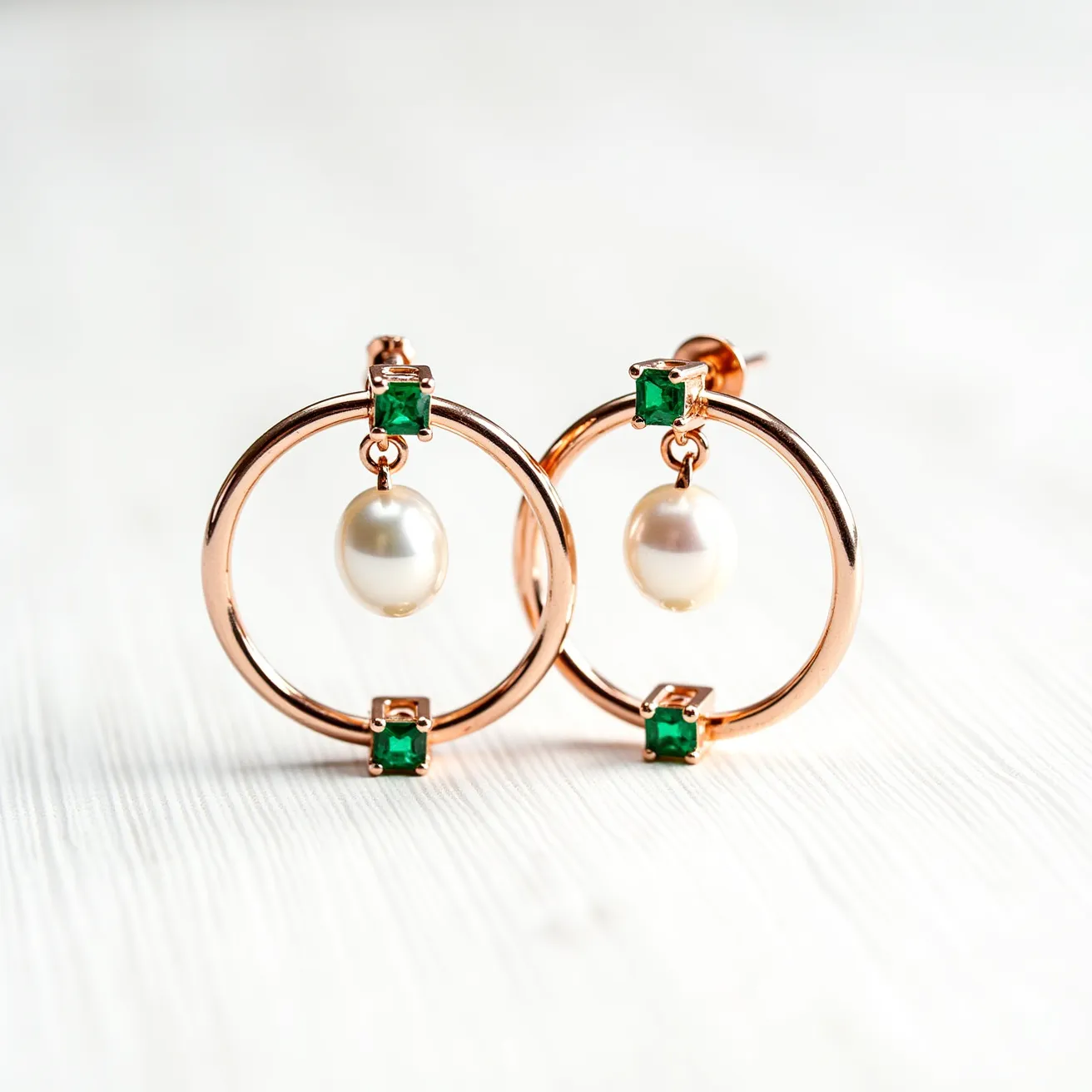 These loop earrings feature a delicate design crafted from a gold-toned metal, forming a perfect circle. Within each loop, a lustrous white pearl dangles gracefully, acting as a captivating focal point. Adjacent to the pearls, a vibrant green gemstone is set at the top and bottom of the circle, adding a complementary pop of color. The gemstones appear to be cut in a rectangular or square shape, securely held by a traditional prong setting. The earrings are equipped with a post back clasp, ensuring they are easy to wear and provide a secure fit.