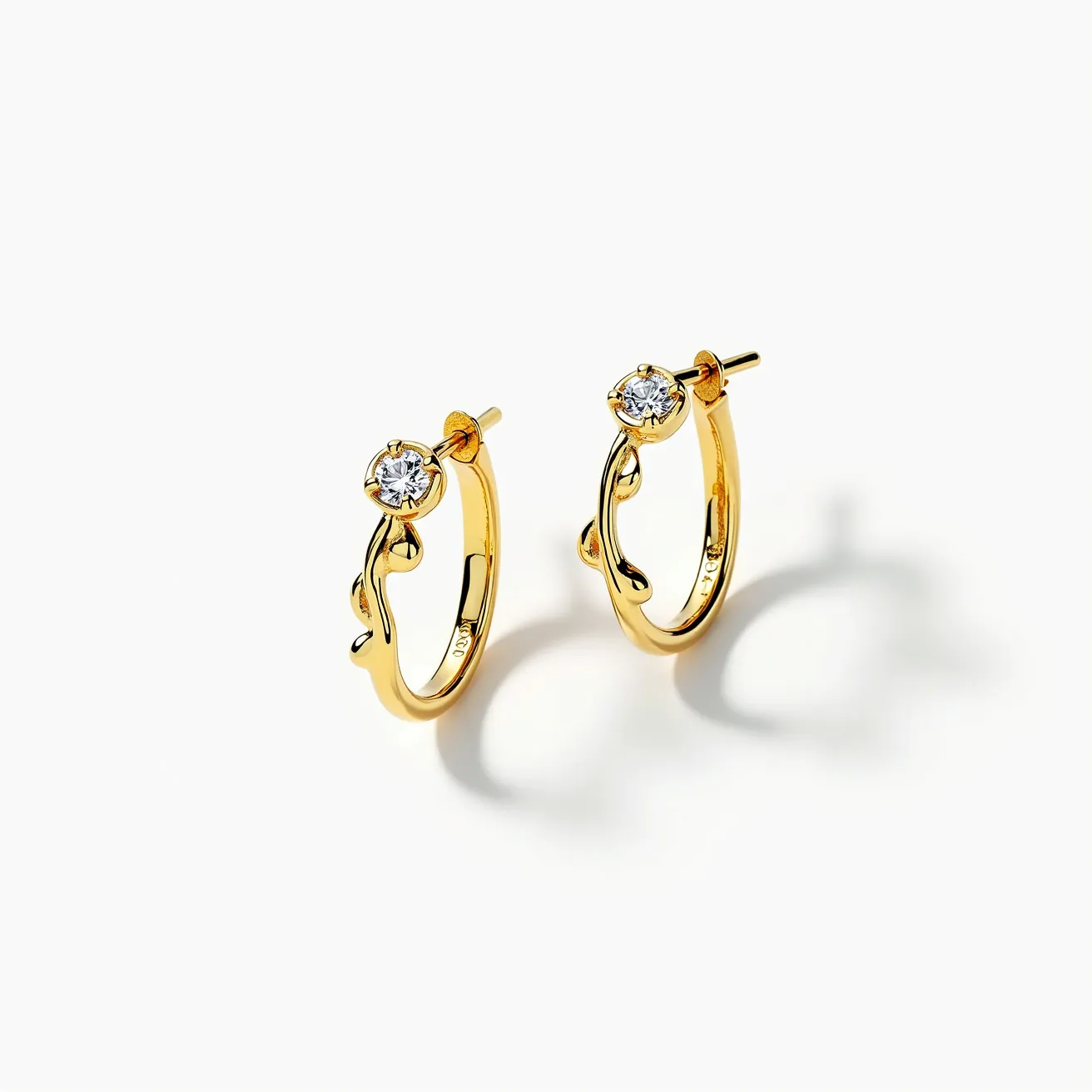 These loop earrings are crafted from a shiny gold material, exhibiting a classic hoop design with an elegant twist. Each earring is adorned with a single round-cut gemstone, likely a diamond, positioned at the top and set in a secure bezel setting, allowing it to catch light from various angles. The clasp features a post style, which is both practical and secure for easy attachment. The gold surface adds a luxurious appeal, highlighting the sleek, polished finish and enhancing the brilliance of the gemstones.