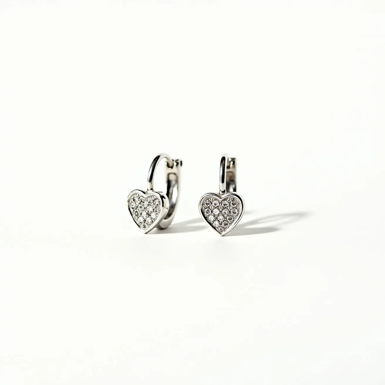 These love earrings feature a polished silver-tone metal design with heart-shaped pendants. Each heart is encrusted with small, round-cut clear gemstones, possibly diamonds or cubic zirconia, set in a pavé style. The earrings are designed with a hinged hoop clasp, providing a secure and elegant attachment to the ear. The craftsmanship highlights a contemporary yet romantic aesthetic, making them suitable for various occasions.