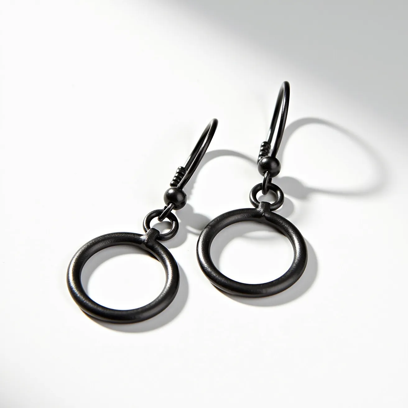 These men's dangle earrings feature a minimalist design with black metal hoops. The circular hoops are sleek and unadorned, emphasizing a contemporary aesthetic. The earrings utilize a simple fishhook attachment, allowing for easy wear and removal while maintaining a secure fit. These earrings are crafted entirely from a dark-toned metal, which provides a subtle yet striking look, suitable for various styles and occasions.