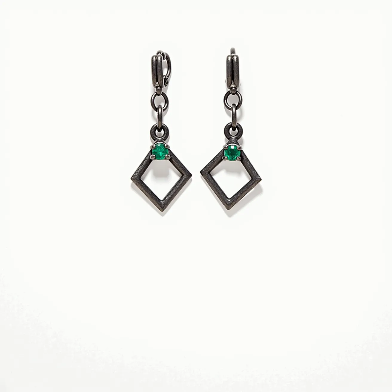 These men's dangle earrings feature a distinctive geometric design, incorporating a diamond-shaped frame crafted from a dark metal that provides a modern and edgy aesthetic. Each earring is adorned with a small, vibrant green gemstone set near the top of the diamond shape, which appears to be an emerald in a classic prong setting, adding a touch of sophistication and color contrast to the overall design. The earrings are attached through a secure clasp mechanism, possibly a hinged hoop or lever-back style, ensuring ease of wear and stability. The combination of the metal and gemstone creates a striking and fashionable accessory suitable for various occasions.