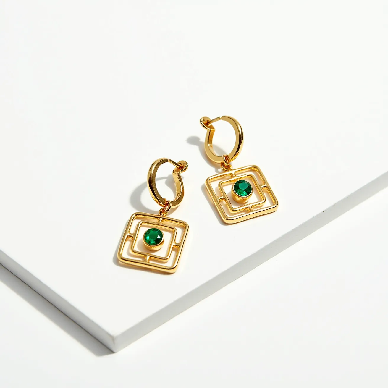 These men's dangle earrings feature a modern and stylish design, crafted from gold-toned metal that forms a geometric square pattern. Each earring is adorned with a vibrant green gem embedded at the center of the square, providing a pop of color and elegance. The green gems are round-cut and bezel-set, enhancing their beauty and ensuring they are securely attached. The earrings utilize hoop clasps for fastening, offering both ease of use and a secure fit.