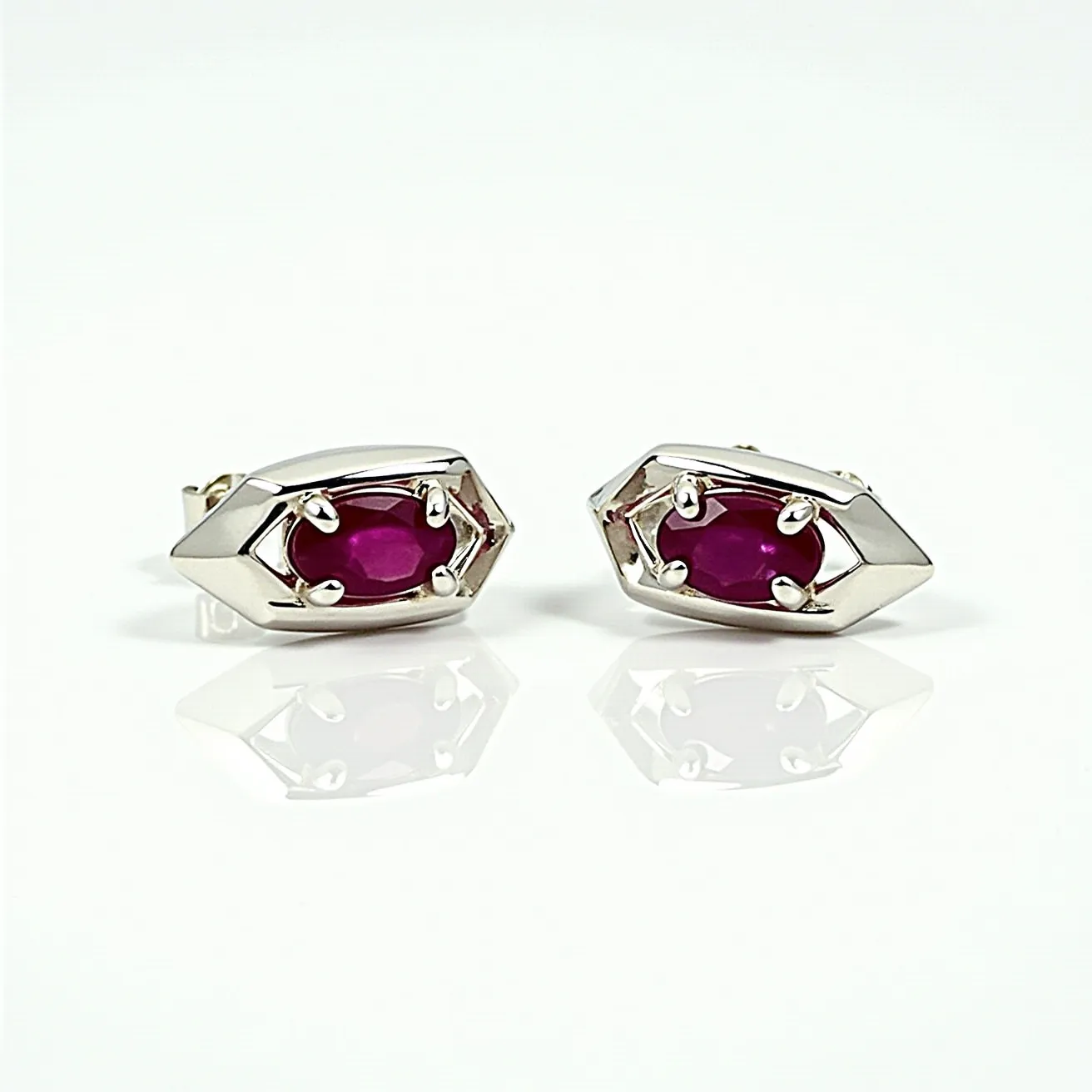 These men's earrings feature an intriguing design composed of a sturdy metal, likely white gold or silver, which forms a hexagonal shape surrounding a central gem. The gem appears to be a vivid red ruby, cut in an oval shape that enhances its deep color and natural luster. The rubies are securely set with a prong setting, allowing light to pass through and reflect off their surfaces, enhancing their brilliance. The earrings are affixed with a post and butterfly clasp, providing secure and comfortable wear. These elements together create an elegant and bold accessory suitable for a sophisticated style.