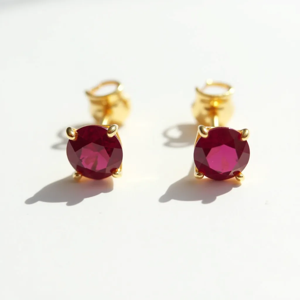 These men's earrings feature round, faceted gemstones with a deep red hue, set in a classic four-prong setting. The metal used for the prongs and post appears to be a gold tone, adding a warm contrast to the vivid red of the stones. These earrings are equipped with a post and butterfly clutch back, which provides secure attachment and ease of use. The overall design is elegant and timeless, suitable for both formal and casual occasions.