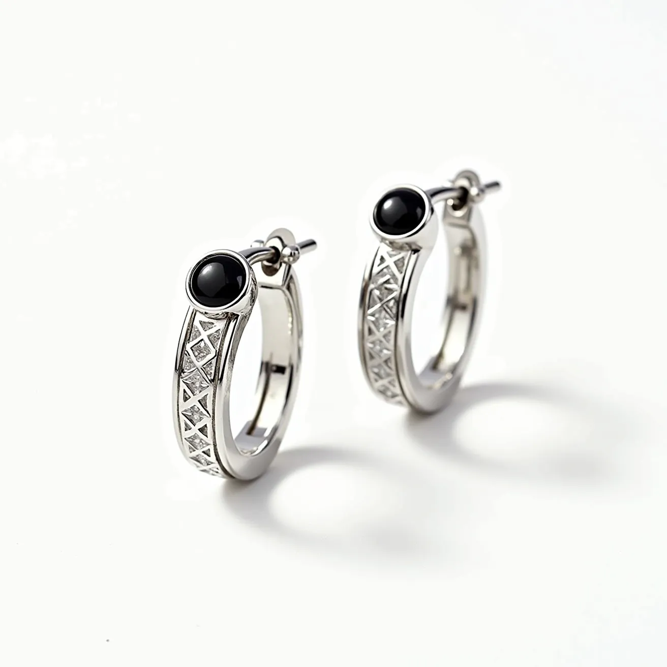 These men's hoop earrings feature a sleek and polished design crafted from what appears to be a high-quality silver metal. Each hoop is adorned with an onyx-like black stone, precisely cut with a smooth and rounded surface, held securely in a bezel setting at the top of the hoop. The body of the earrings showcases an intricate geometric pattern, adding a touch of texture and visual interest. The hoops are equipped with a simple post and latch clasp mechanism for secure attachment, combining both functionality and style.