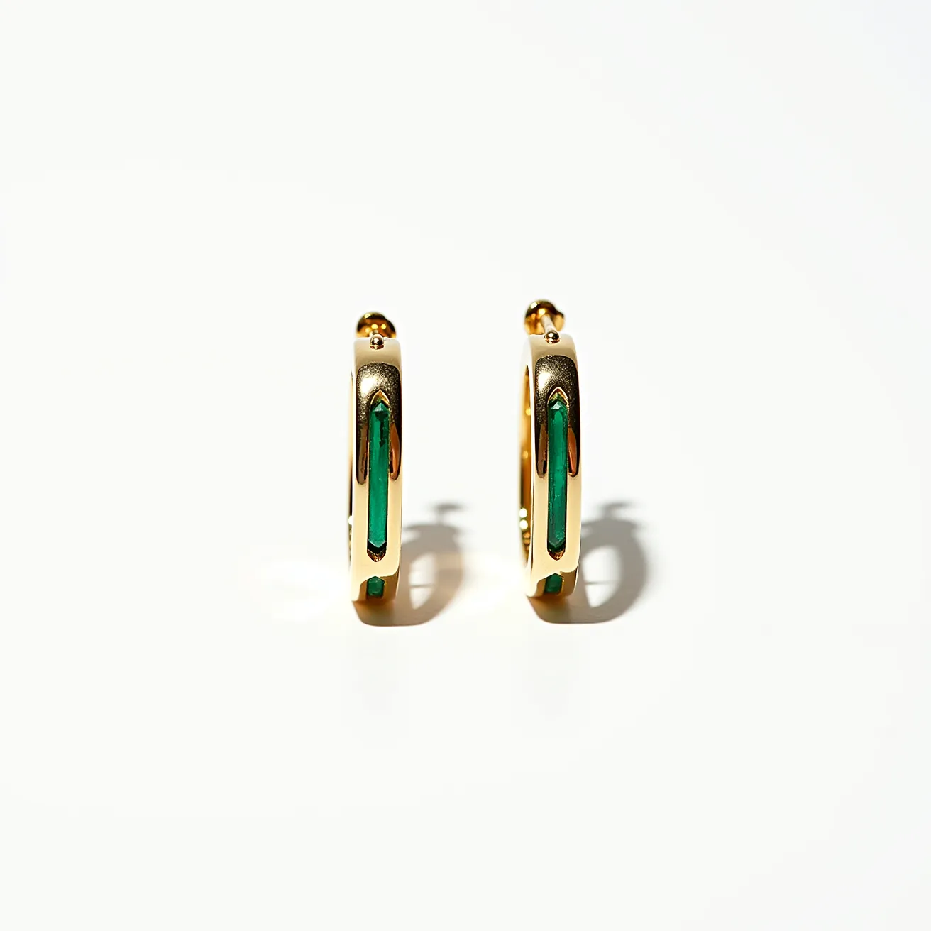 These men's hoop earrings feature a sleek and polished design made from a gold-toned metal, giving them a classic yet stylish appearance. They are adorned with elongated green stones that appear to be set in a channel setting, adding a vibrant touch and contrast to the gold tone. The hoops are designed with a hinge clasp, which offers a secure fastening mechanism and easy wearability. The combination of the green stones and the gold metal creates an elegant and modern aesthetic, making these earrings a chic accessory.