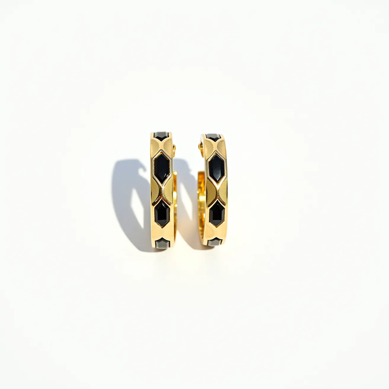 These men's hoop earrings feature a sleek, polished gold material that forms the hoop's base structure. The earrings are adorned with black stones, which are cut into geometric shapes, giving a modern and sophisticated appearance. These stones are set in a pattern that alternates along the outer surface of the hoops, adding visual interest and depth to the design. The earrings utilize a hinge clasp mechanism for secure and convenient attachment, ensuring a comfortable fit for the wearer. The combination of gold and black elements presents a striking contrast that enhances the overall elegance of the piece.