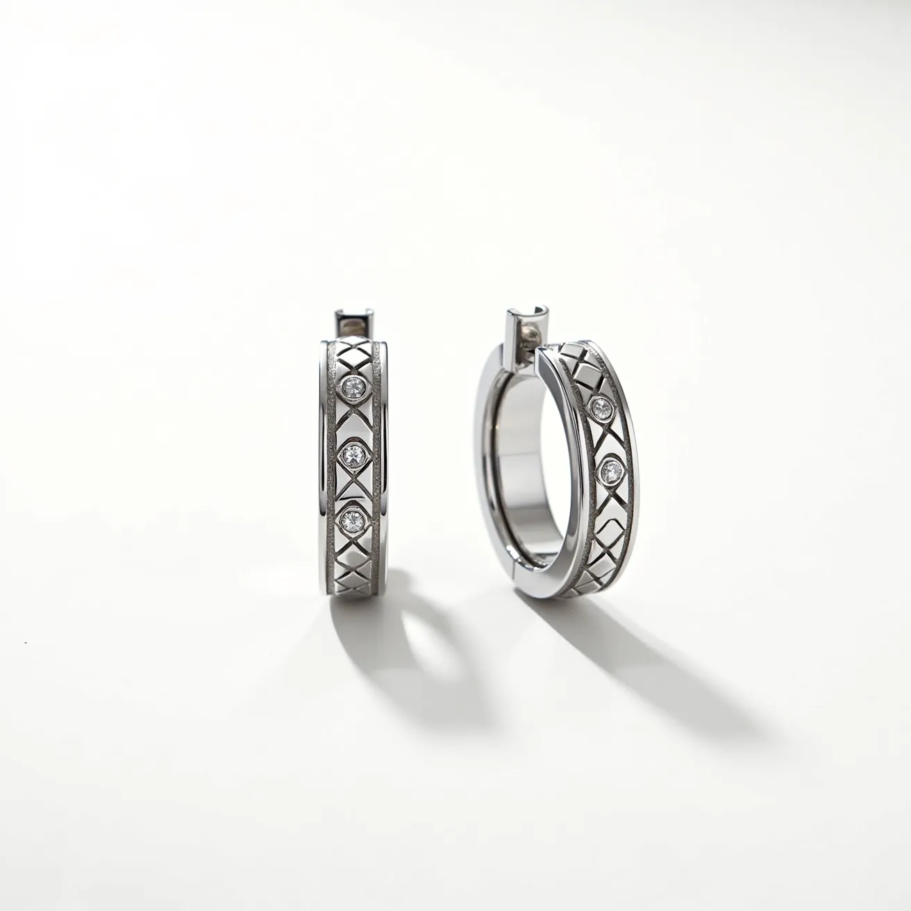 These men's hoop earrings are crafted from a polished metal, likely stainless steel or a similar alloy, giving them a sleek and modern appearance. They feature a row of small, round cut gems set within the hoops. The gems are secured in a bezel or flush setting, adding a subtle touch of elegance. The design includes an intricate pattern engraved along the surface, enhancing the aesthetic appeal. These earrings utilize a hinged snap closure, ensuring a secure and comfortable fit when worn.