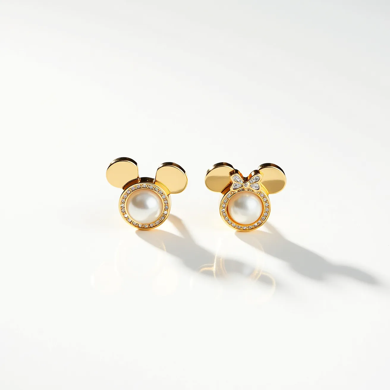 These Mickey Mouse earrings feature a charming design crafted from polished gold-toned metal, highlighting the iconic silhouette of Mickey's ears. The central element of the earring showcases a round, lustrous pearl, which is surrounded by a sparkling array of small, clear stones that may be diamonds, set in a pavé setting to add an elegant sparkle. The right earring is adorned with a delicate bow above the pearl, crafted from the same small stones. The earrings are likely secured with a post and butterfly clasp, providing a secure and comfortable fit for the wearer.