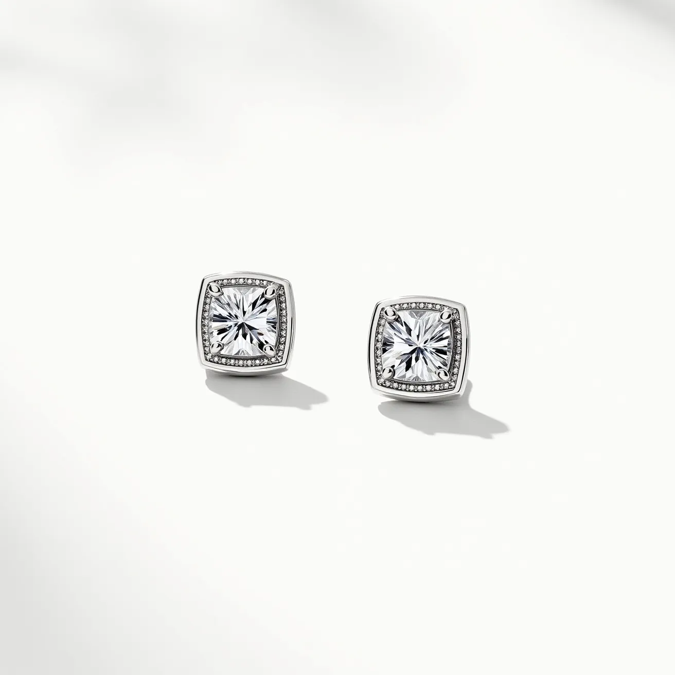 These moissanite earrings showcase a striking square-cut moissanite stone, set in a sleek metal frame likely made of white gold or platinum, enhancing its elegant appearance. The central gem is surrounded by smaller, delicately arranged moissanite stones, creating a halo effect that adds to its brilliance. The secure setting ensures the stones are prominently displayed, enhancing their reflective qualities with a modern aesthetic. The earrings are designed as studs, featuring a simple post-back closure for ease of wear and a timeless look, suitable for various occasions and styles.