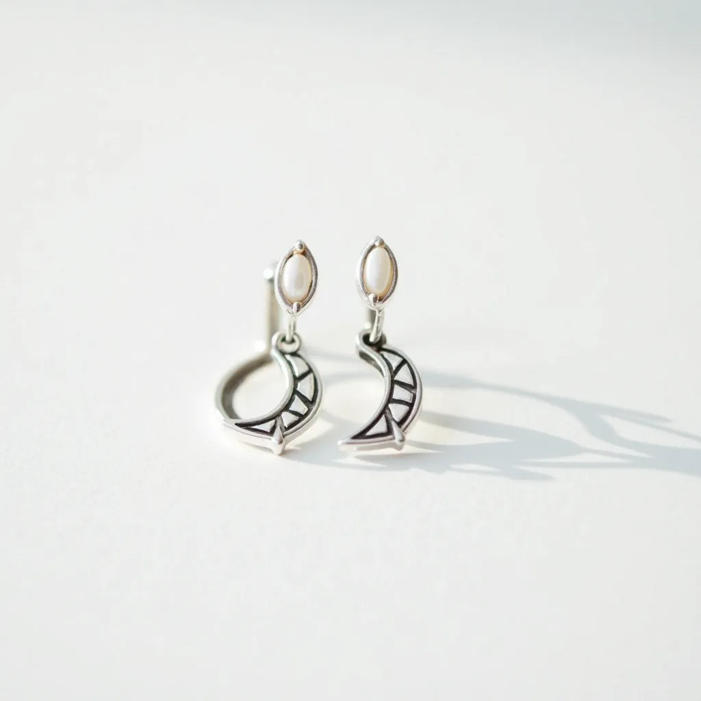 These moon earrings are crafted from a shiny metal, likely silver, with sleek, minimalist crescent moon shapes as the main feature. Above each moon is an oval-shaped gem with a smooth surface, possibly resembling a pearl or a similarly lustrous stone, set in a bezel setting that securely holds the gem. The earrings are designed with a post back attachment, ensuring easy wear and secure fastening. The crescent moons are adorned with openwork detailing, adding a modern and sophisticated touch to the overall design.