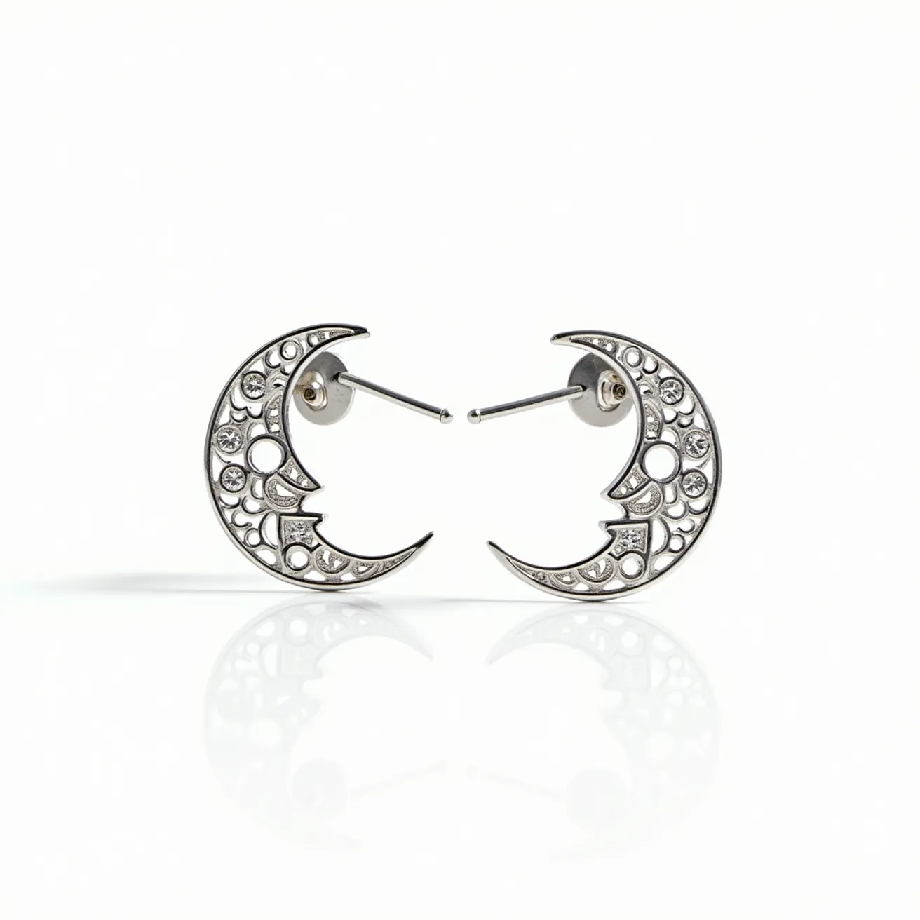 These moon earrings are crafted from a shiny metal, possibly silver or white gold, and feature a crescent shape. The surface is adorned with small, round clear gems, likely diamonds or cubic zirconia, set in a bezel setting, which enhances their sparkle. The design includes decorative cut-outs that add to the celestial theme. The earrings are designed for pierced ears, utilizing a post and push-back clasp for secure attachment. The overall aesthetic is elegant and intricate, capturing the ethereal appeal of the moon.