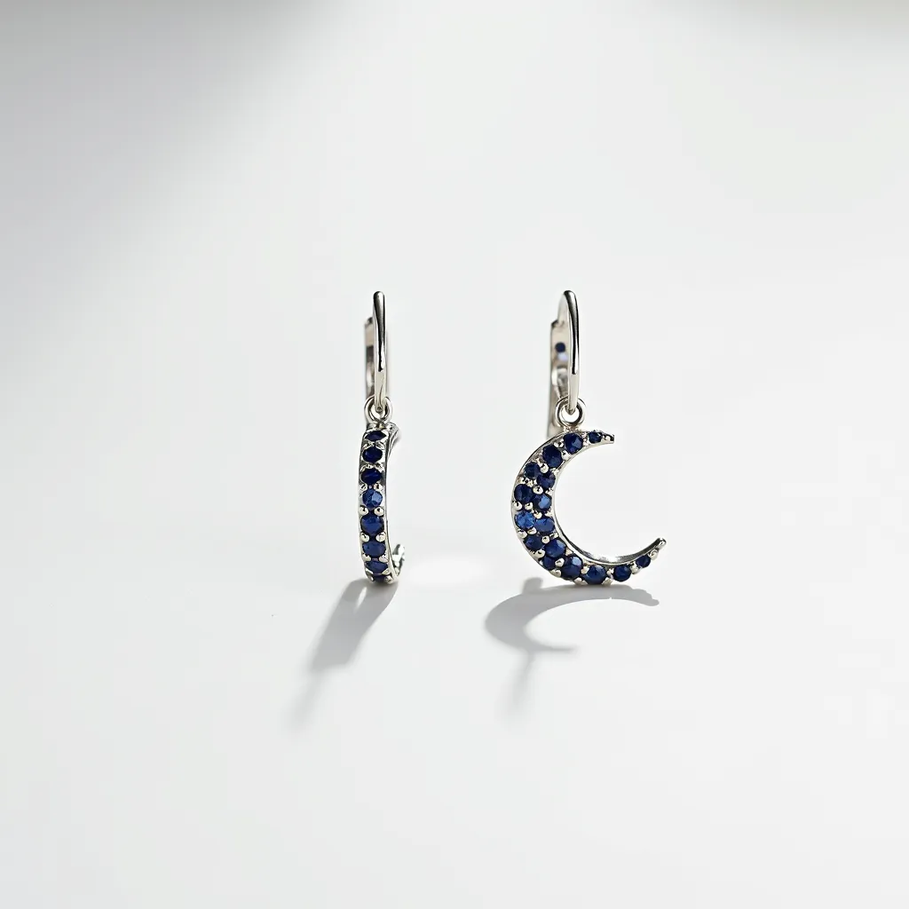 These moon earrings feature a crescent moon design adorned with small, round-cut blue gemstones that are precisely set along the curve of each earring, adding a celestial sparkle. The earrings are crafted from a lustrous silver-toned metal that contrasts beautifully with the deep blue of the gems. Each earring is attached via a lever-back clasp, ensuring a secure fit while adding a touch of elegance to the overall design. The combination of the materials and the fine detailing contribute to the earrings' sophisticated and whimsical aesthetic.