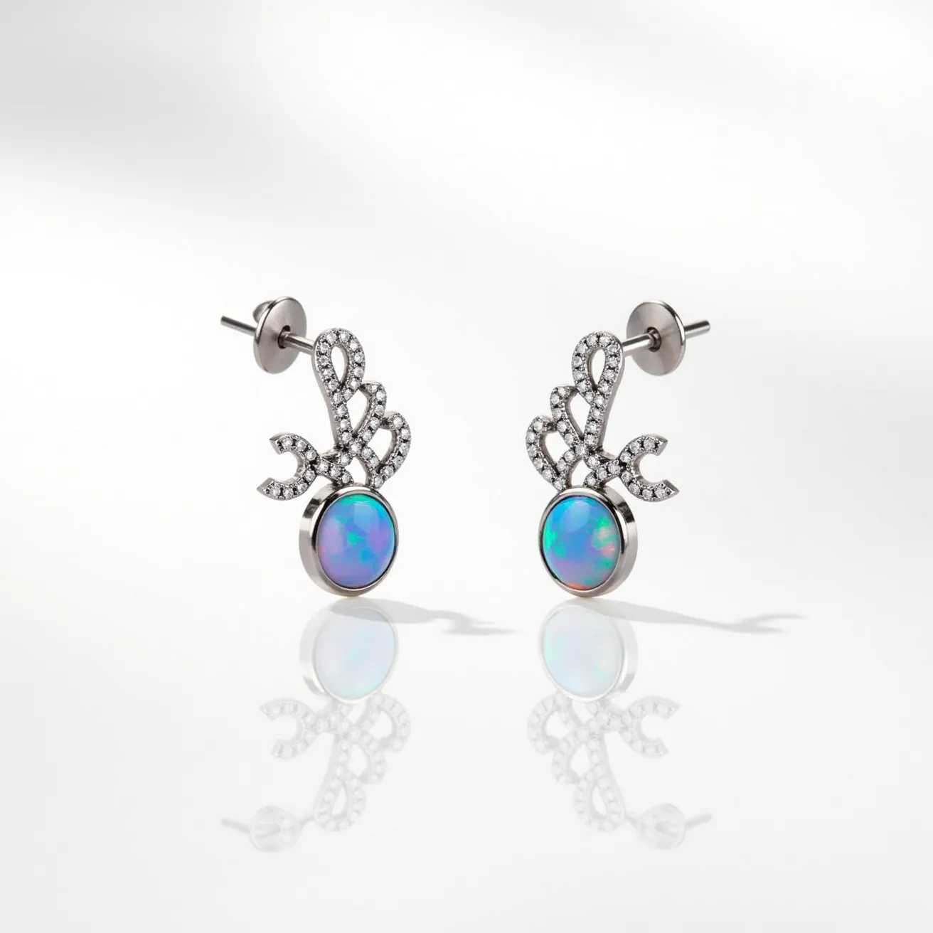 These opal earrings feature a captivating design with prominently set opals that exhibit a vibrant play of colors, characteristic of fine opals. The stones are cabochon cut, emphasizing their smooth, domed surfaces. Surrounding the opal is a sophisticated arrangement of small, sparkling diamonds that are pave-set, forming an elegant swirl or leaf-like motif. The metal appears to be a polished white gold or platinum, enhancing the brilliance of the diamonds and providing a sleek, modern backdrop for the opals. The earrings are designed to be worn with a post and butterfly clutch fastening, ensuring a secure and comfortable fit.