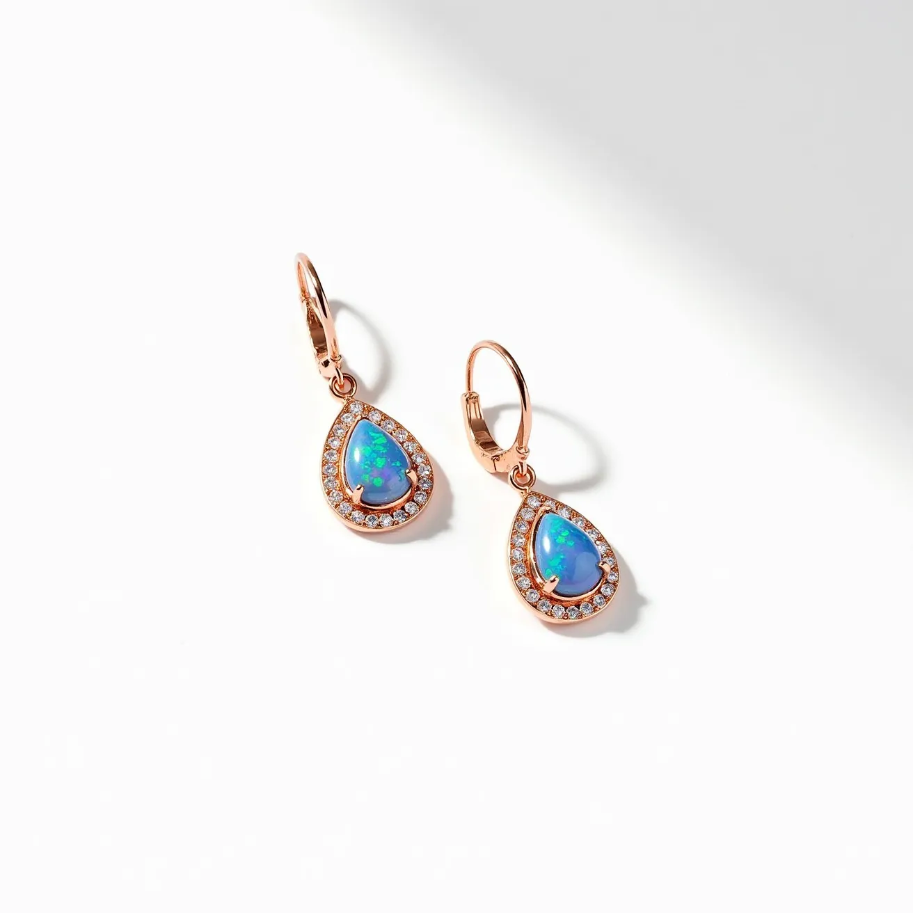 These opal earrings feature a stunning teardrop-shaped opal set in a bezel of rose gold. The opal displays a vibrant play of color, showcasing hues of blue, green, and hints of yellow. Encircling the opal is a halo of small, round-cut diamonds, adding a sparkling contrast to the design. These stones are meticulously set in a pave style, enhancing the overall elegance of the earrings. The earrings are attached to a lever-back clasp, providing a secure mechanism that complements the sophisticated style. The combination of opal, diamonds, and rose gold creates a harmonious and luxurious piece of jewelry.