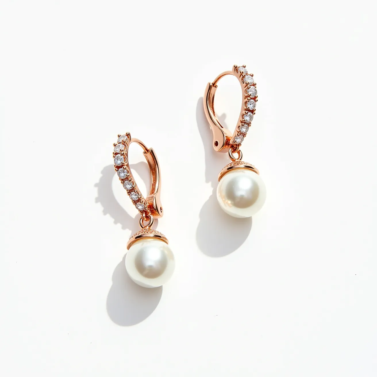 These pearl drop earrings feature elegant round pearls suspended from a rose gold setting. Each earring is adorned with a row of sparkling, small round-cut diamonds set along the front of the rose gold lever-back clasps, providing a secure closure while adding a touch of glamour. The pearls have a smooth, lustrous surface, complementing the brilliance of the diamonds. The combination of pearls and diamonds in a rose gold setting gives these earrings a timeless and sophisticated appeal.