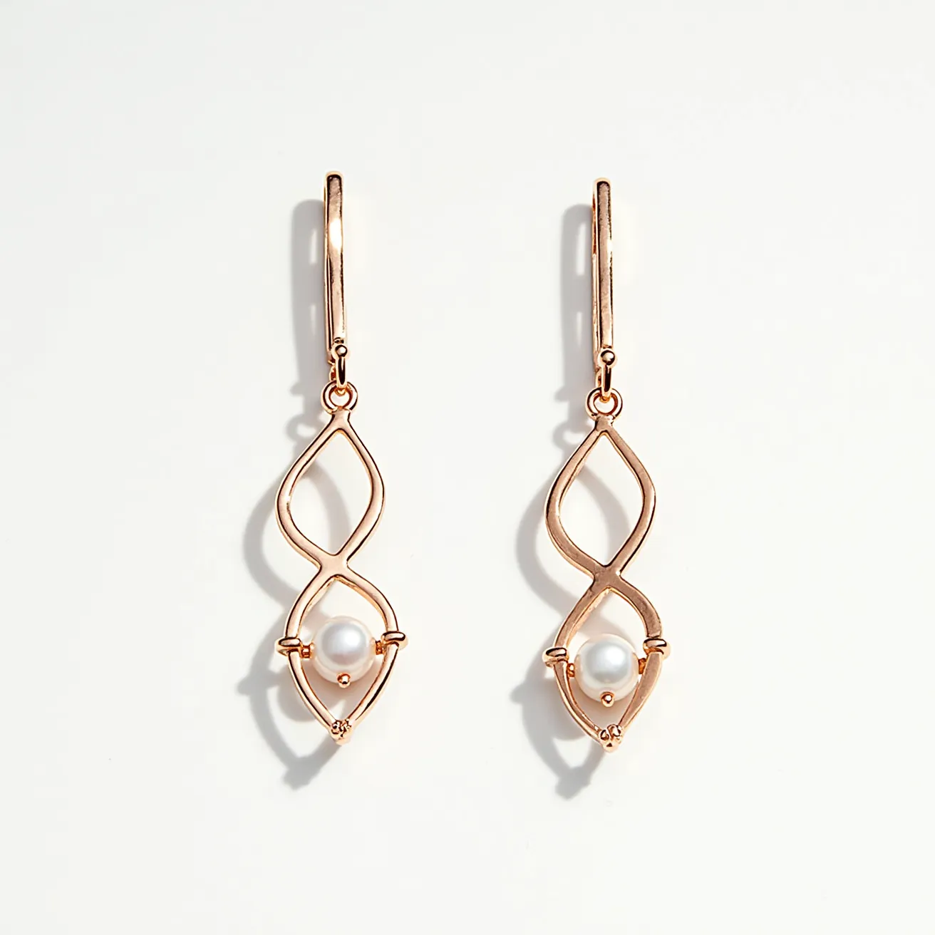 These pearl drop earrings feature a sophisticated design with a delicate, rose gold metal framework shaped into an elegant, elongated open loop. Each earring is adorned with a single round pearl, securely set at the bottom of the loop, adding a touch of classic elegance. The pearls sit in a bezel-like setting, emphasizing their lustrous, smooth surface. The earrings are attached with simple lever-back clasps, ensuring a secure fit while contributing to the overall graceful and refined appearance. The combination of the shimmering pearls and the warm tone of the rose gold creates a balanced and stylish accessory ideal for both everyday wear and special occasions.