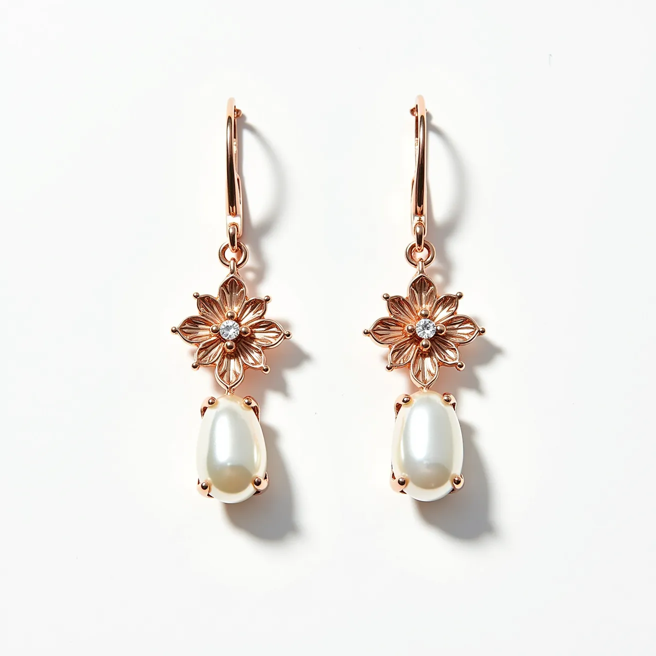 These pearl drop earrings feature a sophisticated design incorporating lustrous pearls as the focal point, elegantly held in place by a rose gold-toned prong setting. The earrings are adorned with intricately crafted floral motifs that add artistic flair, each centered with a small, sparkling gemstone, possibly a diamond, in a brilliant cut. These earrings are suspended from lever-back clasps that provide a secure and comfortable wear. The combination of pearls, delicate floral elements, and a gemstone accent creates a harmonious blend of elegance and charm.